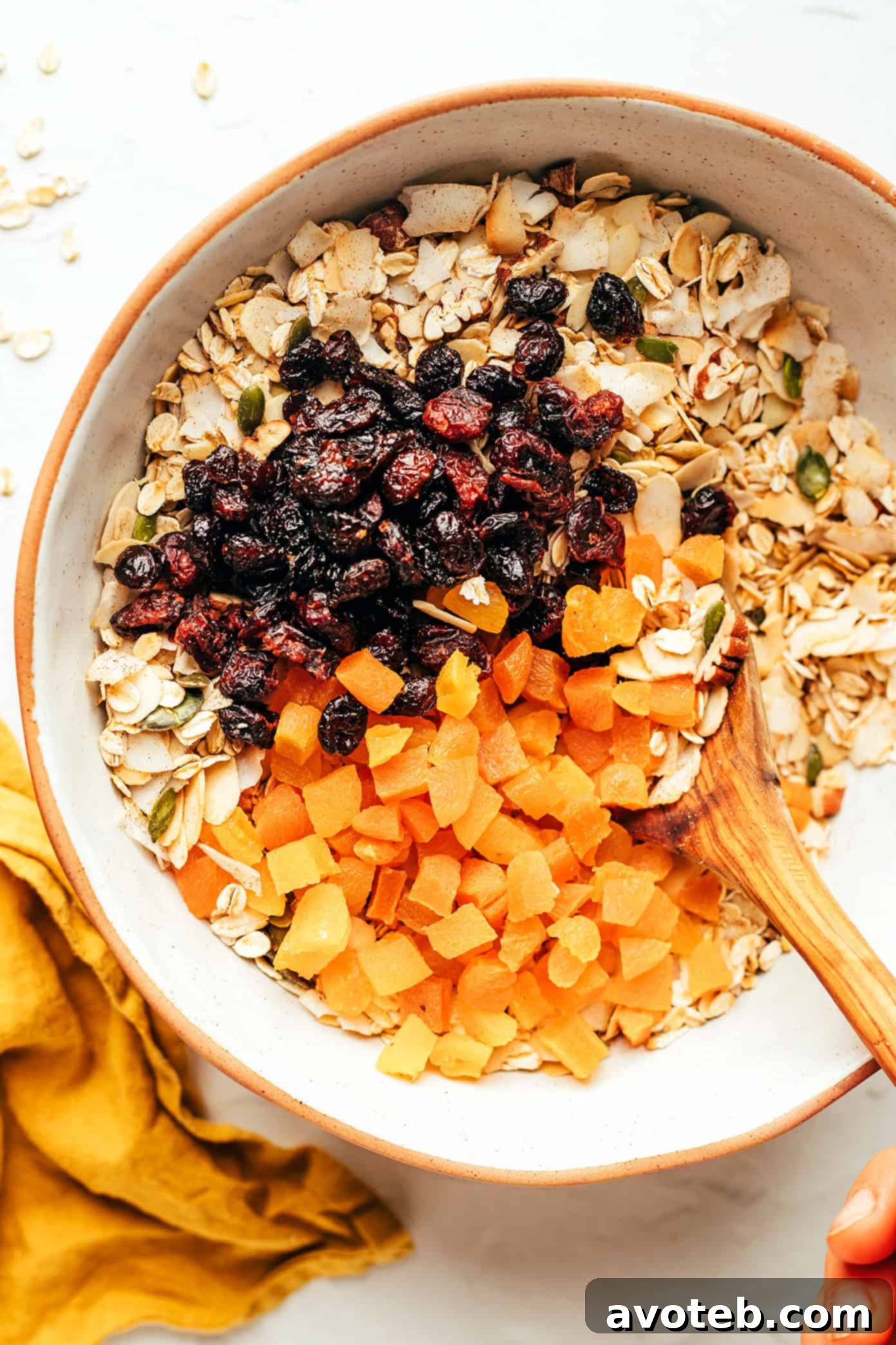 This delicious homemade muesli recipe is easy to make and customize with your favorite blend of oats, nuts, seeds, dried fruit, coconut (optional) and spices. Serve with hot or cold milk, prep "overnight oats"-style, layer as a parfait with Greek yogurt, or however you love best. Always such a great healthy and easy breakfast! | gimmesomeoven.com Close-up shot of dry muesli ingredients, including oats, various nuts, seeds, and spices, mixed together in a large white mixing bowl, ready for the next step in preparation.