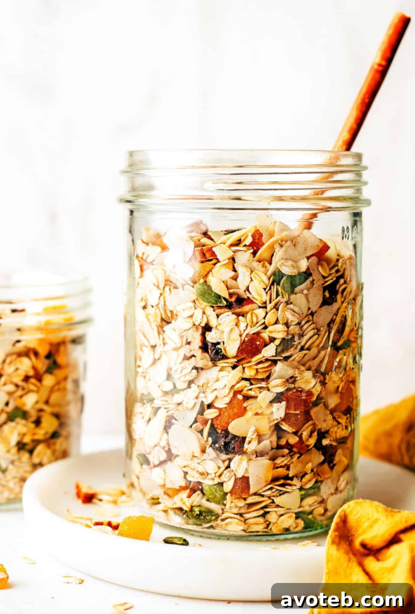 This delicious homemade muesli recipe is easy to make and customize with your favorite blend of oats, nuts, seeds, dried fruit, coconut (optional) and spices. Serve with hot or cold milk, prep "overnight oats"-style, layer as a parfait with Greek yogurt, or however you love best. Always such a great healthy and easy breakfast! | gimmesomeoven.com A tall glass jar filled to the brim with homemade muesli, showcasing the layered texture of oats, various nuts, seeds, dried fruits, and coconut, ready for storage or serving.