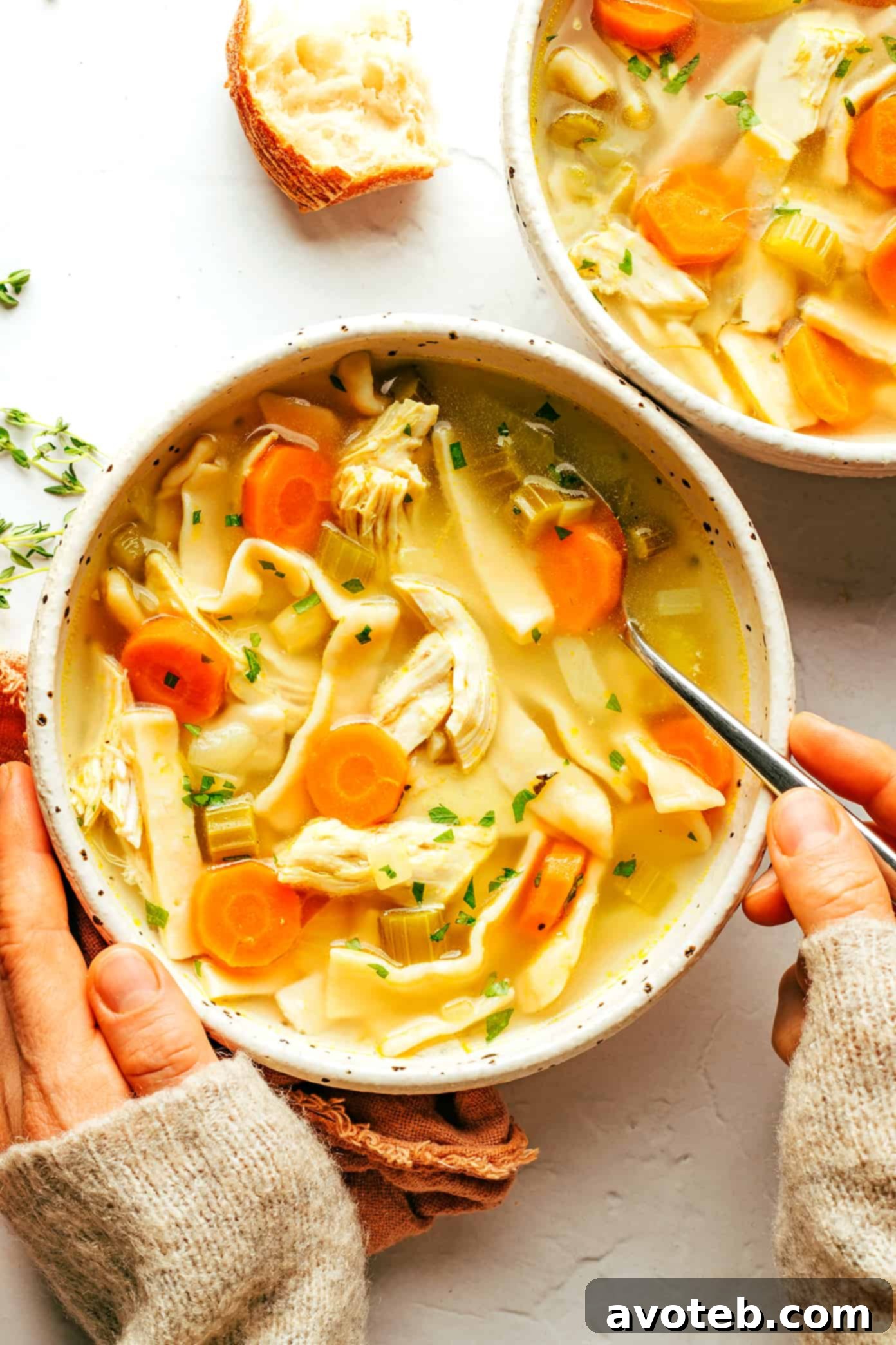 Bowls of homemade chicken noodle soup, garnished with fresh parsley, served with crusty bread.