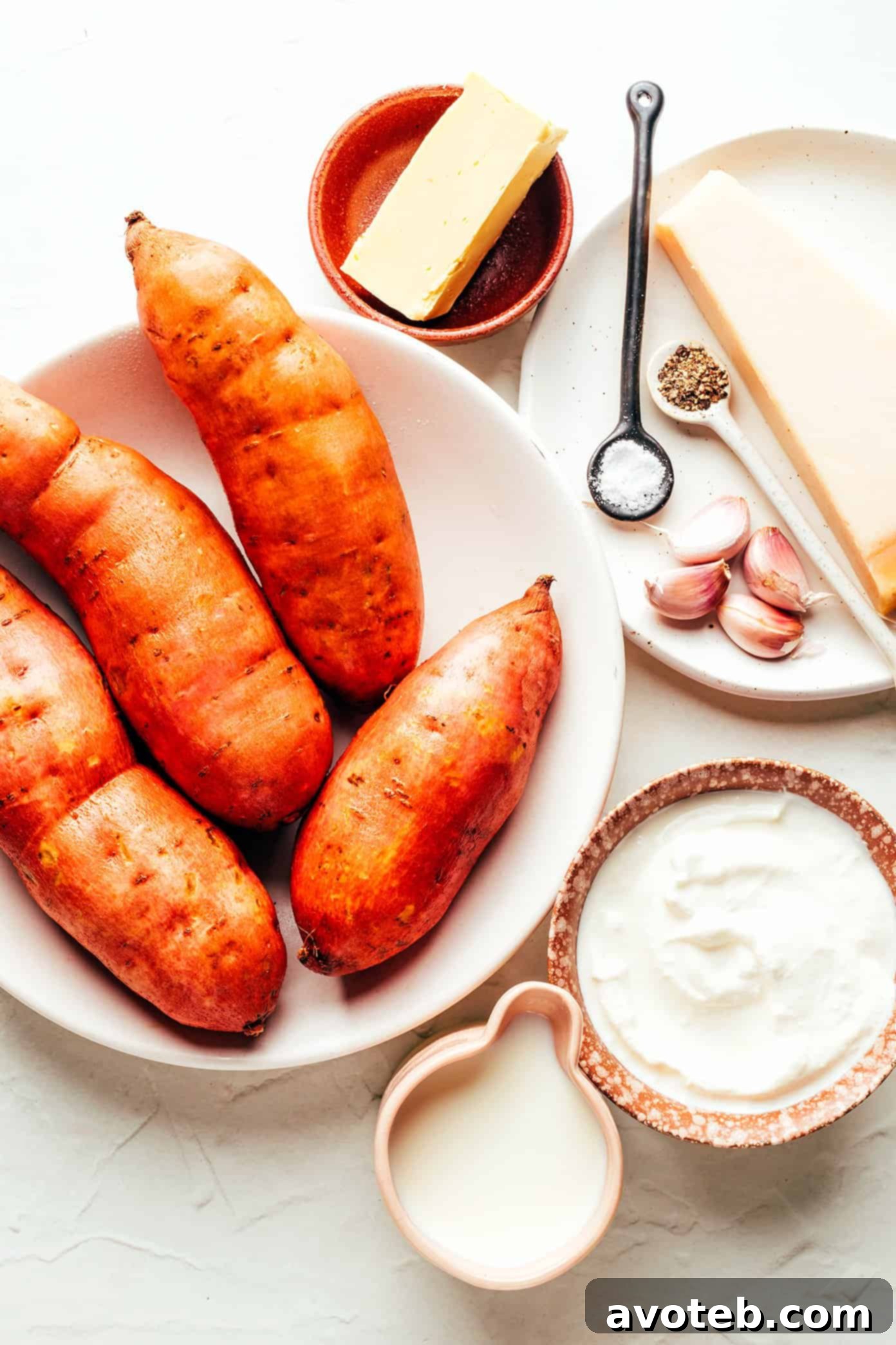 A vibrant display of fresh ingredients for Garlic Parmesan Mashed Sweet Potatoes, including sweet potatoes, garlic, Parmesan cheese, chives, butter, milk, and sour cream.