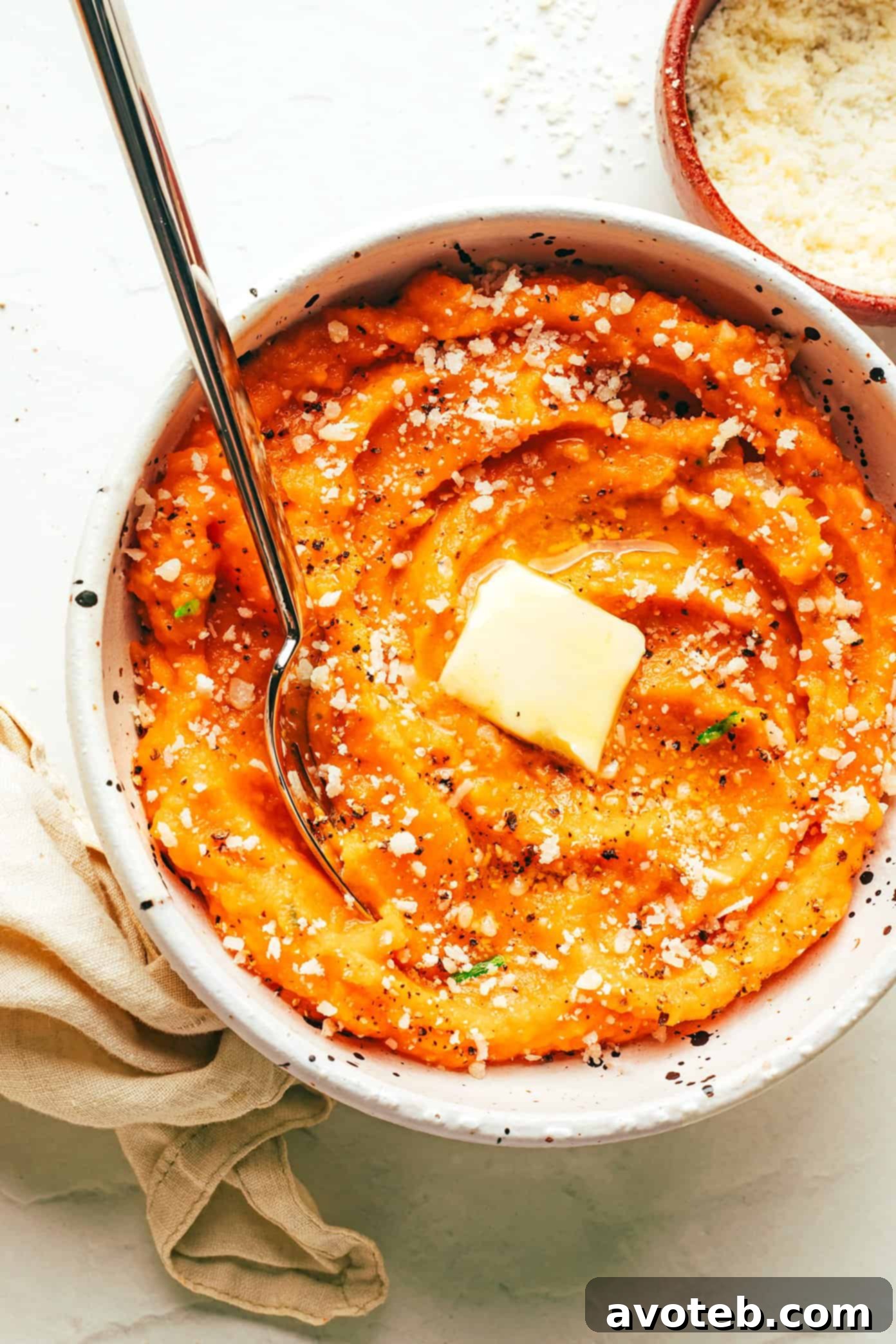 A serving of Garlic Parmesan Mashed Sweet Potatoes in a bowl, with a pat of butter melting on top, garnished with fresh herbs.