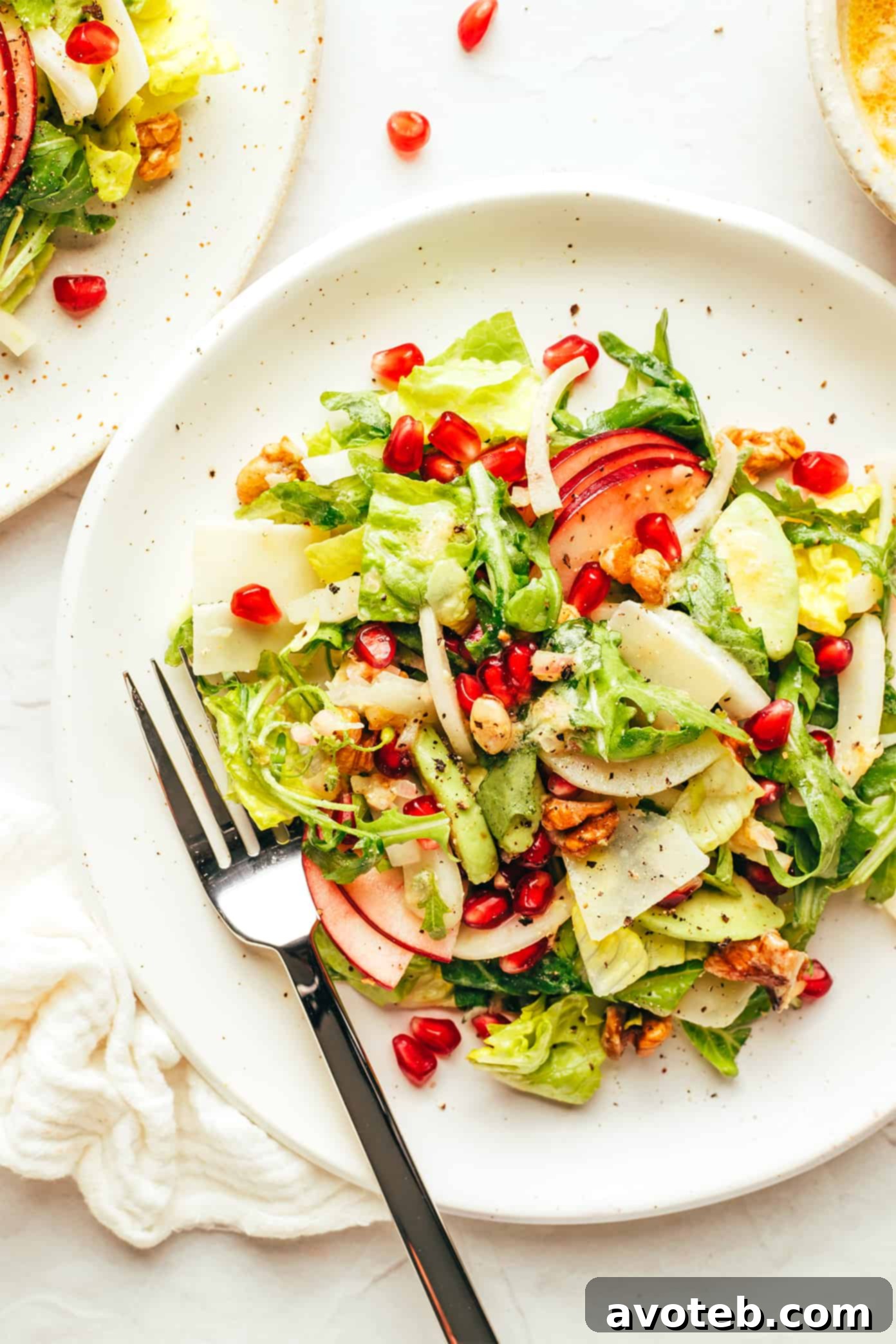 A close-up view of the exquisite Christmas salad, showcasing its vibrant ingredients: crisp apple, ruby pomegranate arils, savory Parmesan, and crunchy walnuts. Close-up of a delightful Christmas Salad on a plate, featuring apple, pomegranate, Parmesan, and walnuts