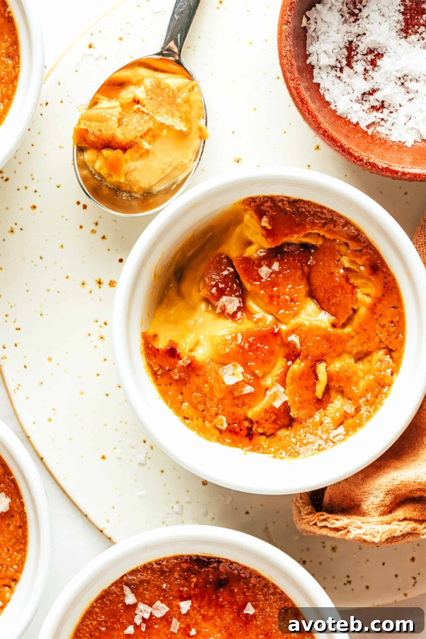 Experience the delightful crack of the sugar crust and the creamy salted caramel custard. Salted Caramel Crème Brûlée with a spoon breaking the sugar crust
