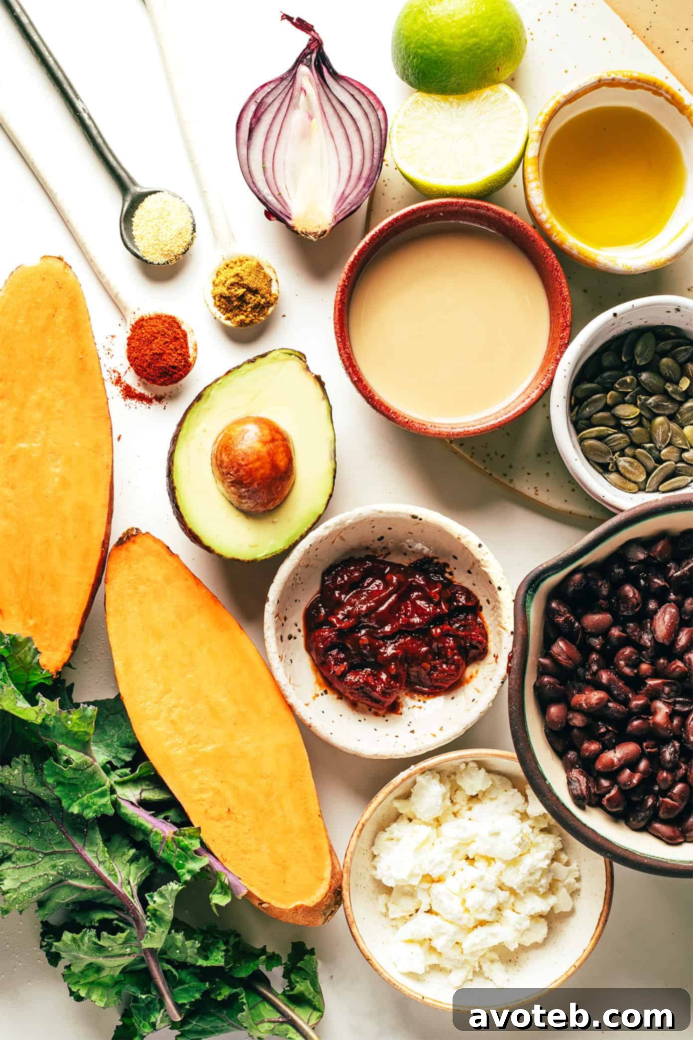 Ingredients for Sweet Potato Avocado Kale Salad with Chipotle Tahini Dressing laid out on a surface, showcasing fresh produce like sweet potatoes, kale, avocado, red onion, cilantro, black beans, and the components for the tahini dressing.