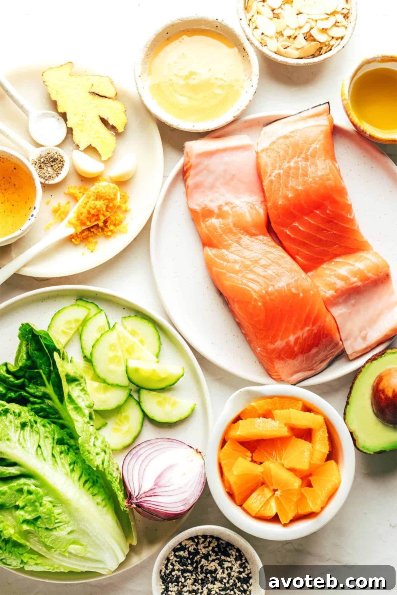 Fresh ingredients for Orange Salmon Salad laid out on a cutting board, including salmon fillets, oranges, avocado, cucumber, red onion, and romaine lettuce.