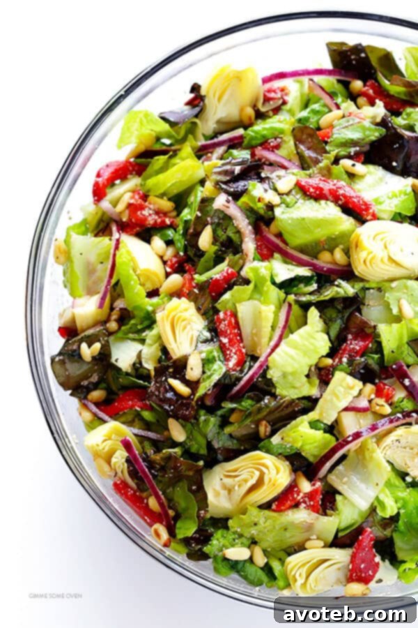 Fresh salad ingredients, including crisp greens, artichokes, red peppers, and pine nuts, being tossed in a large bowl before dressing.