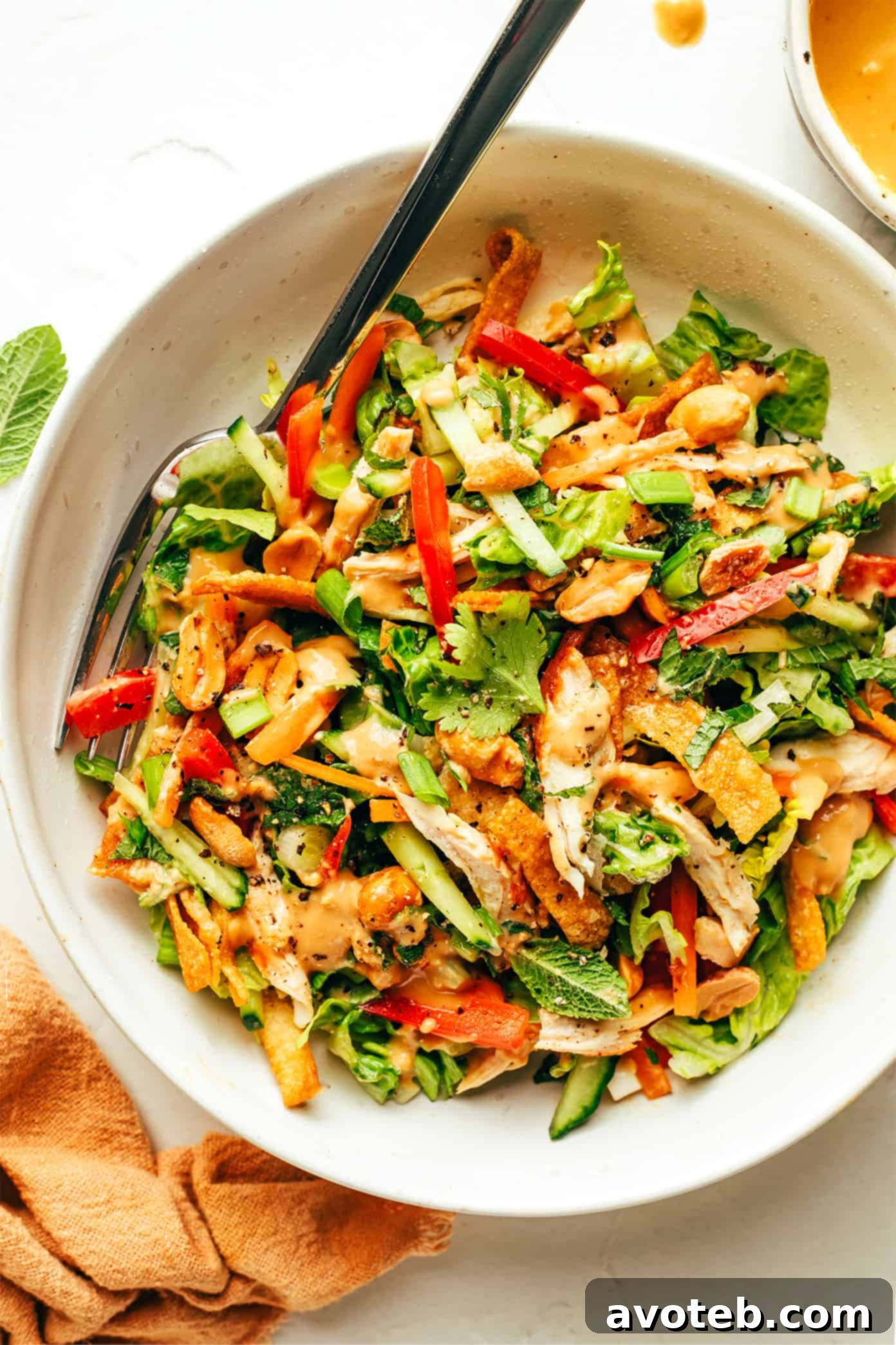 Thai Crunch Salad in a bowl with a fork, generously drizzled with peanut dressing