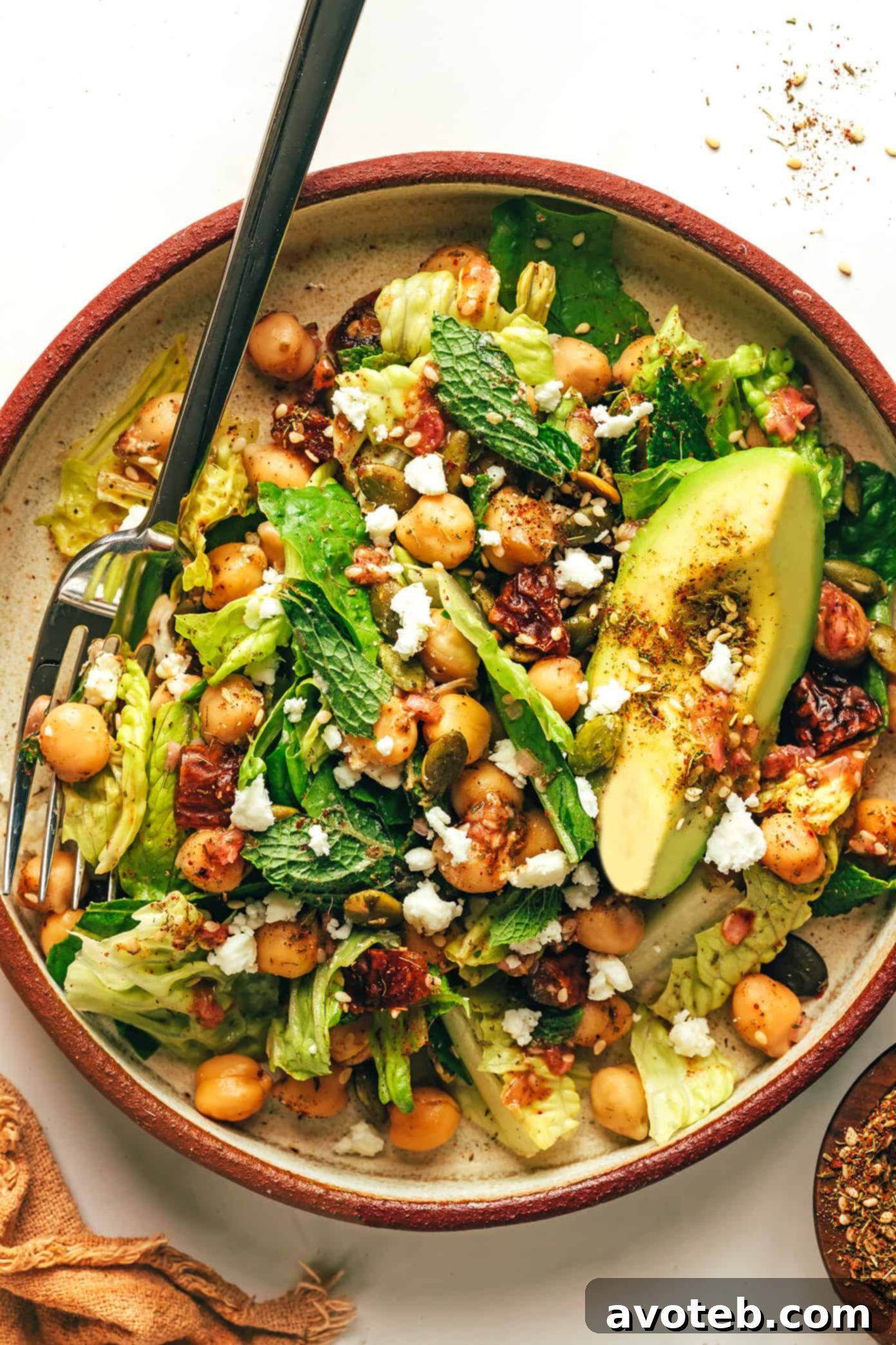 This vibrant green salad is loaded up with chickpeas, Medjool dates, avocado, pepitas, loads of fresh mint, and tossed with a lemony za'atar shallot vinaigrette. It's naturally vegan and gluten-free, but feel free to add a protein such as chicken, steak, shrimp or salmon if you'd like. So fresh and delicious! | gimmesomeoven.com Close-up of Chickpea, Date, and Avocado Salad with Za'atar Vinaigrette in a serving bowl with a fork