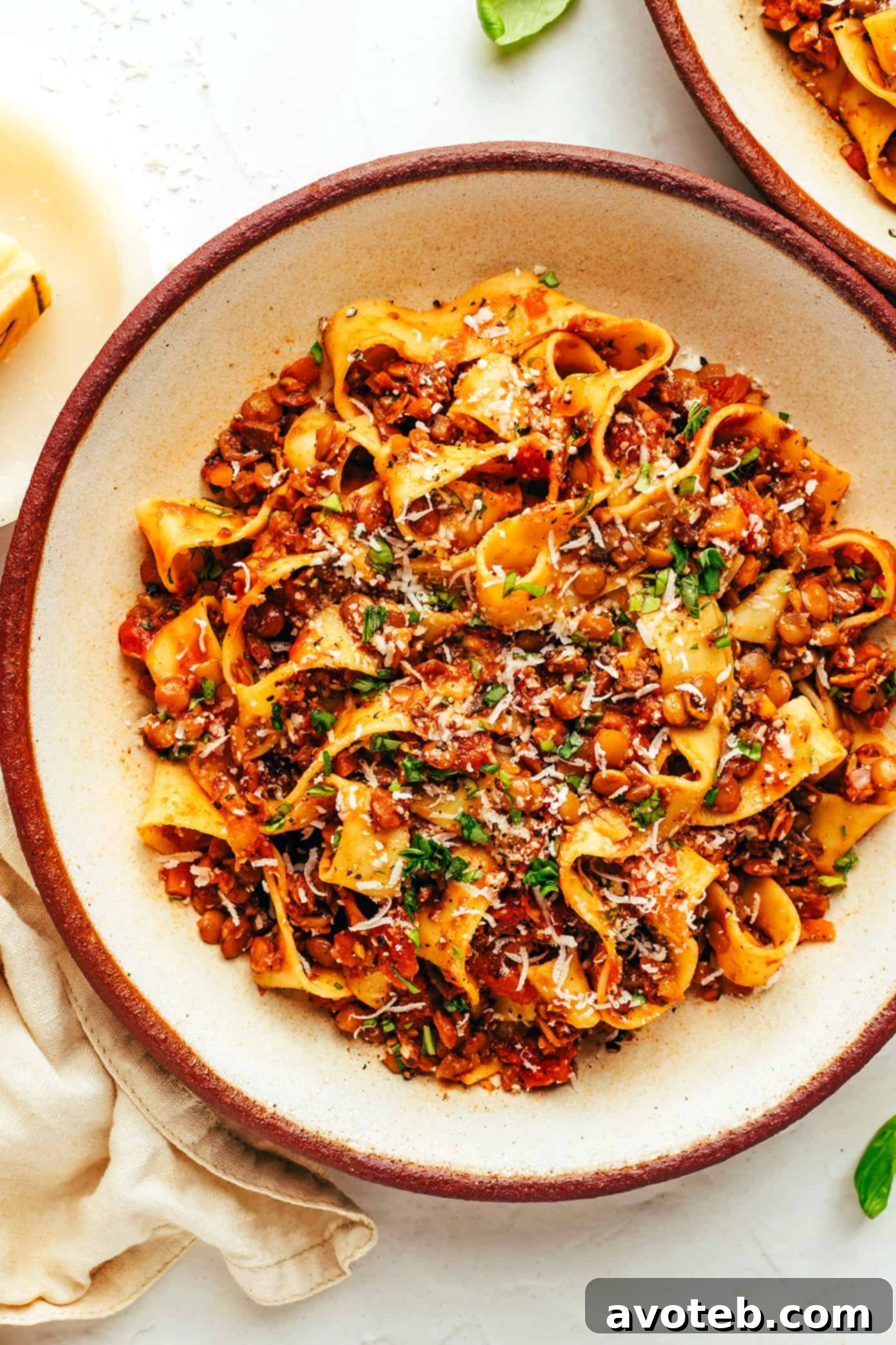 A beautifully plated bowl of vegetarian bolognese with pasta, generously topped with freshly grated parmesan and vibrant basil, ready to be enjoyed. Vegetarian bolognese with pasta, parmesan and basil in bowl