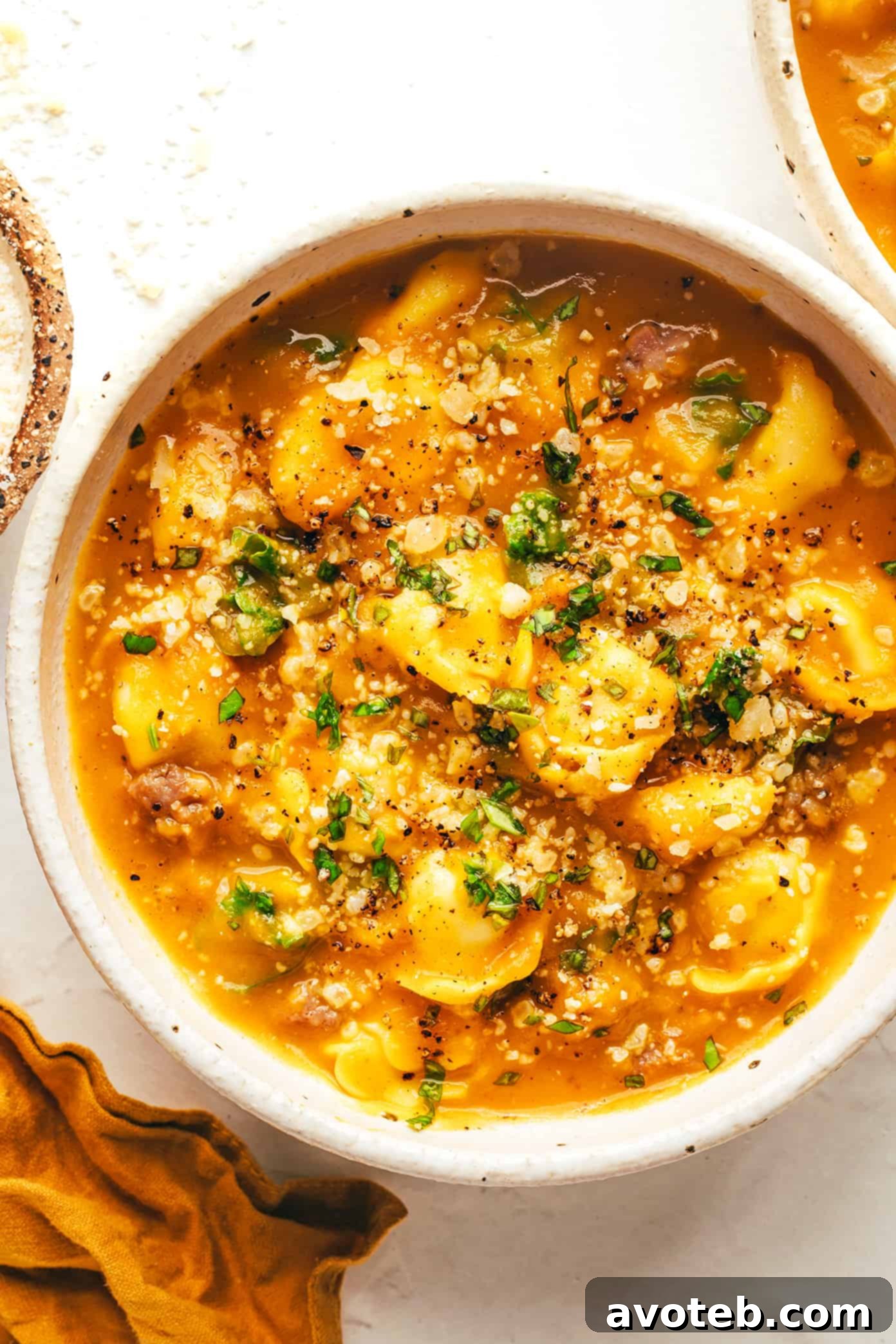 A steaming bowl of butternut squash, sausage, and tortellini soup garnished with fresh herbs and Parmesan, served on a wooden surface.