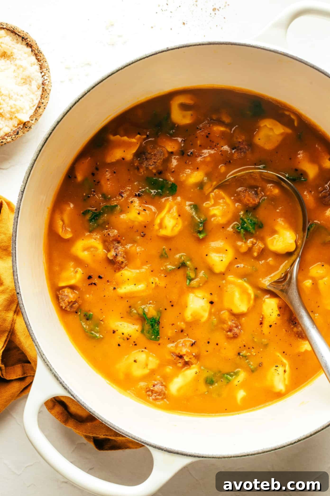 A close-up of a serving of butternut squash, sausage, and tortellini soup, showing the texture of the tortellini and kale.