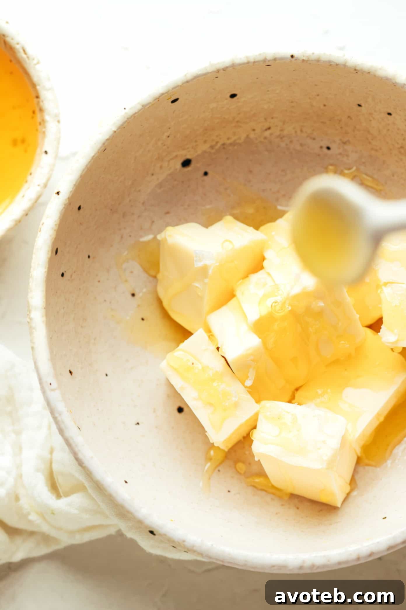 A mixing bowl with butter, honey, and salt being whipped together with a hand mixer, creating a fluffy texture.