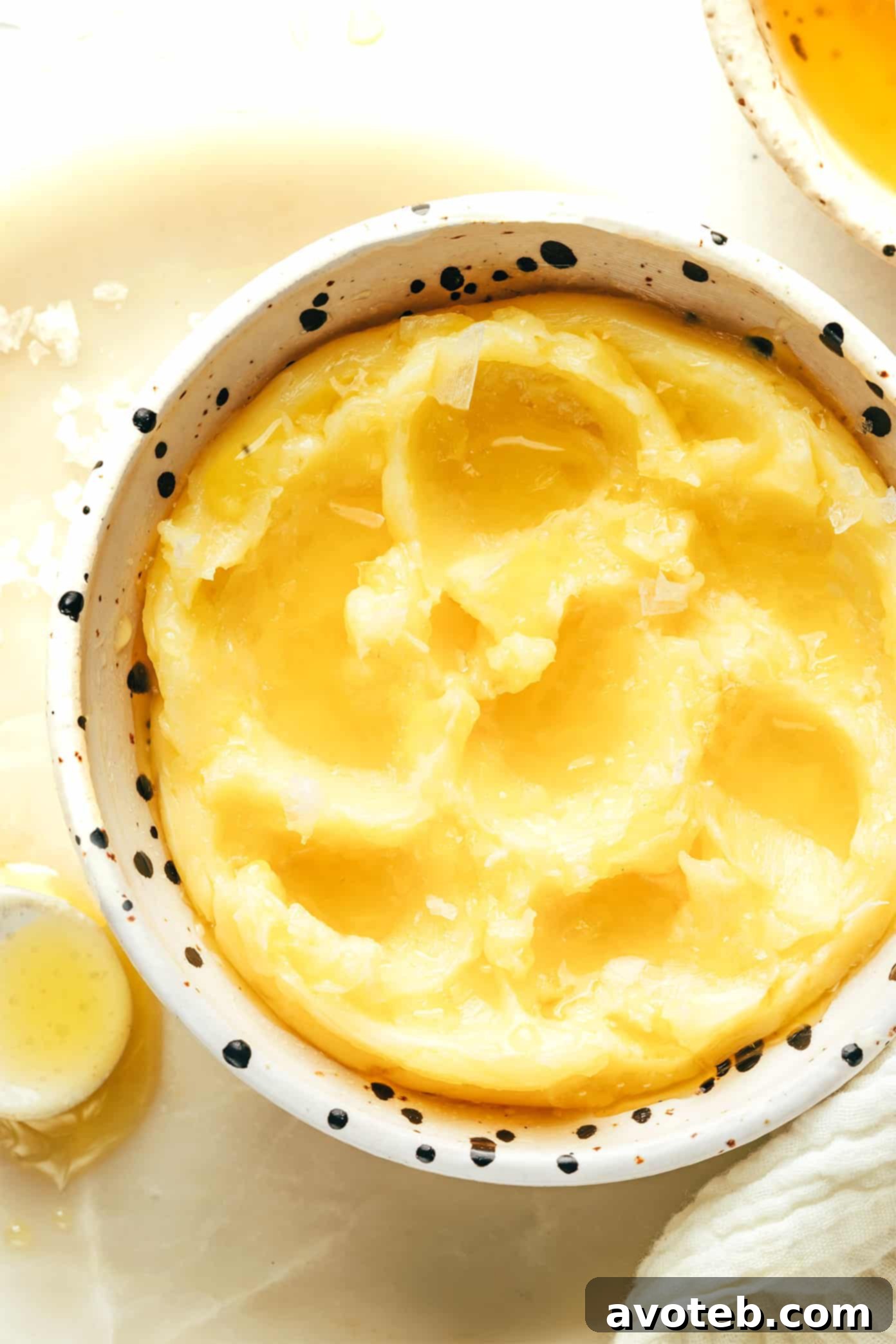A small jar of honey butter, garnished with flaky sea salt, next to a stack of golden brown pancakes.