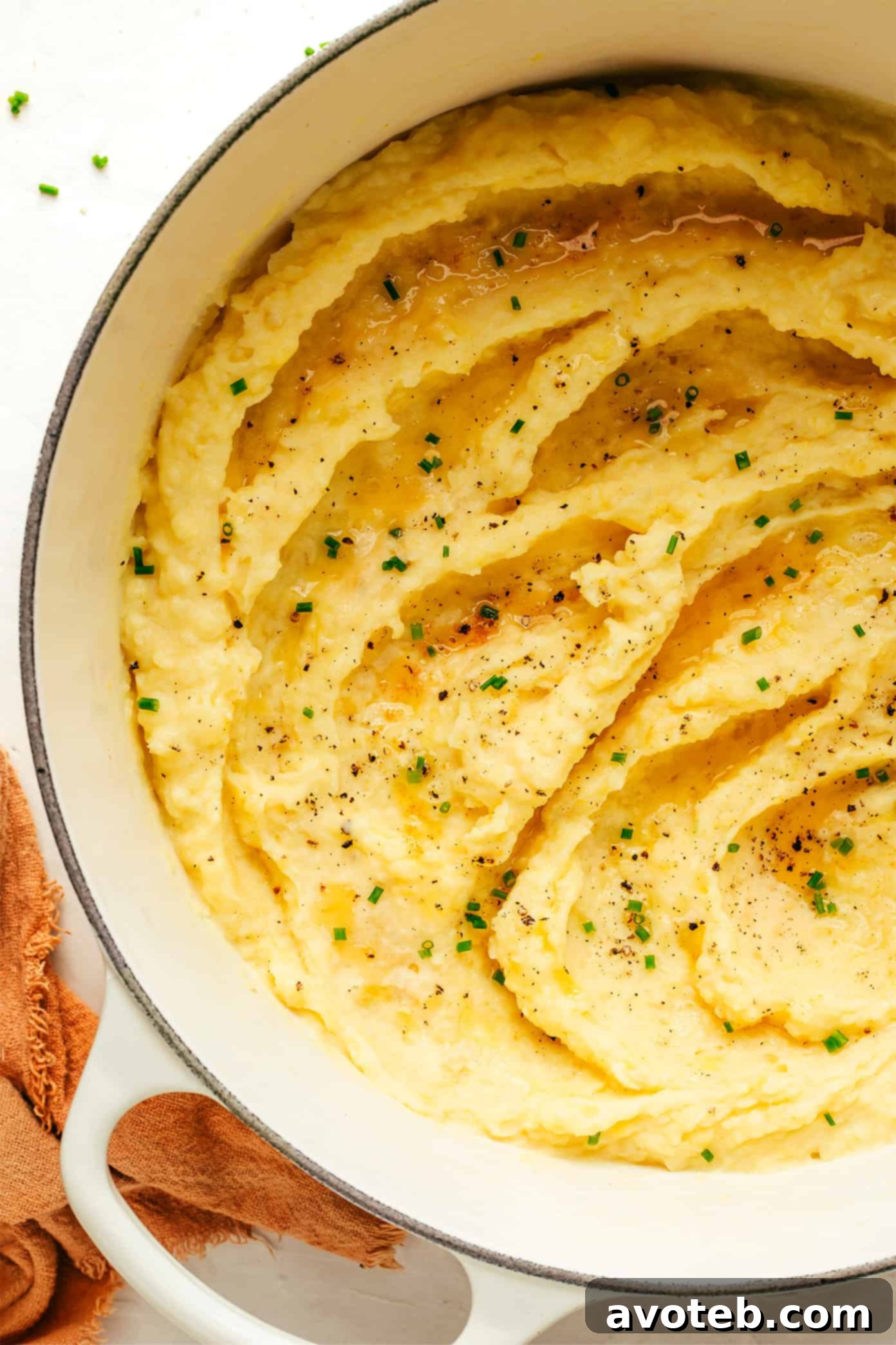 Golden Nutty Potato Mash 5 A white serving bowl filled with brown butter mashed potatoes, adorned with a sprig of fresh herbs.
