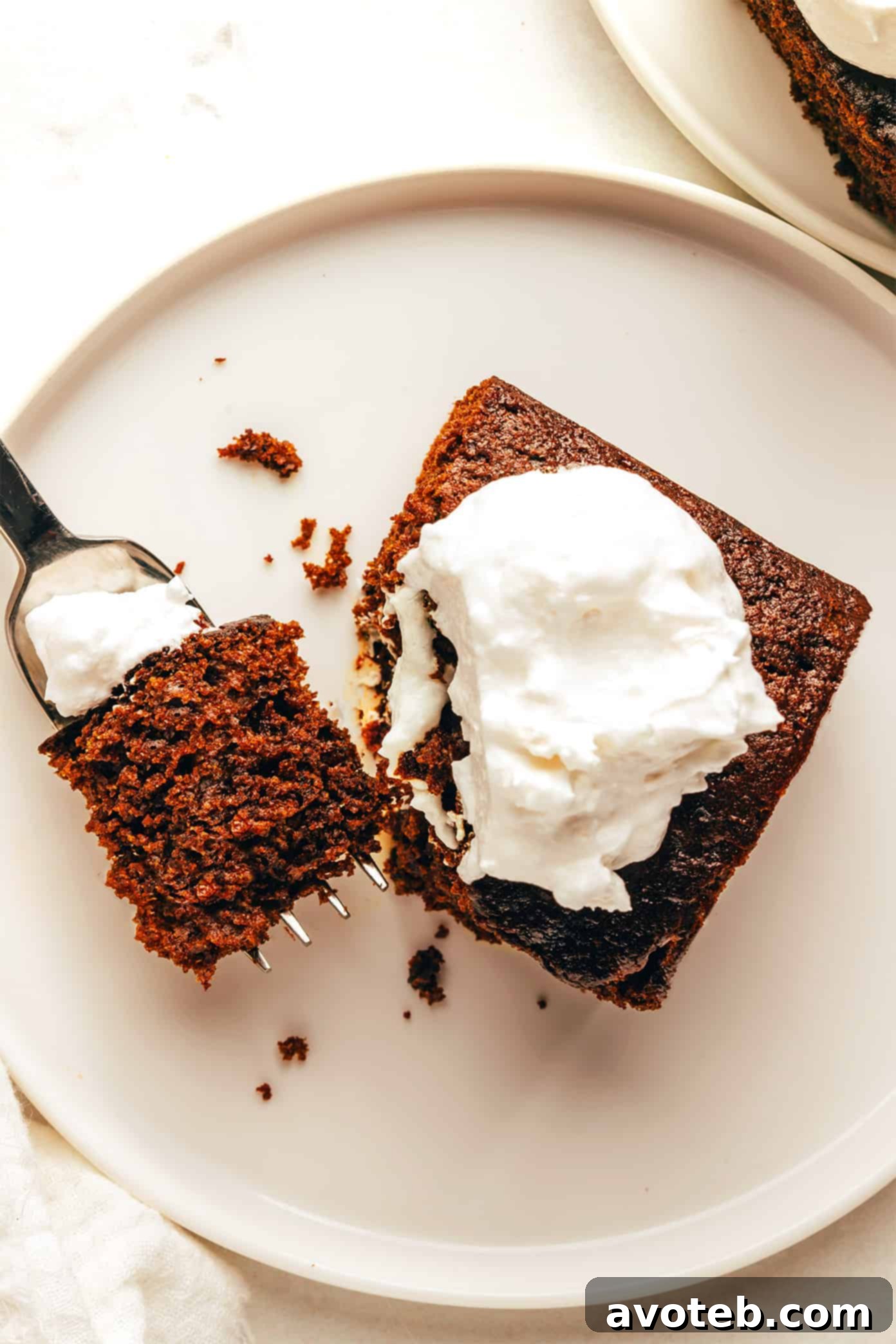 A close-up of a generous slice of gingerbread cake, revealing its rich, moist interior, with a fork poised to take a bite.