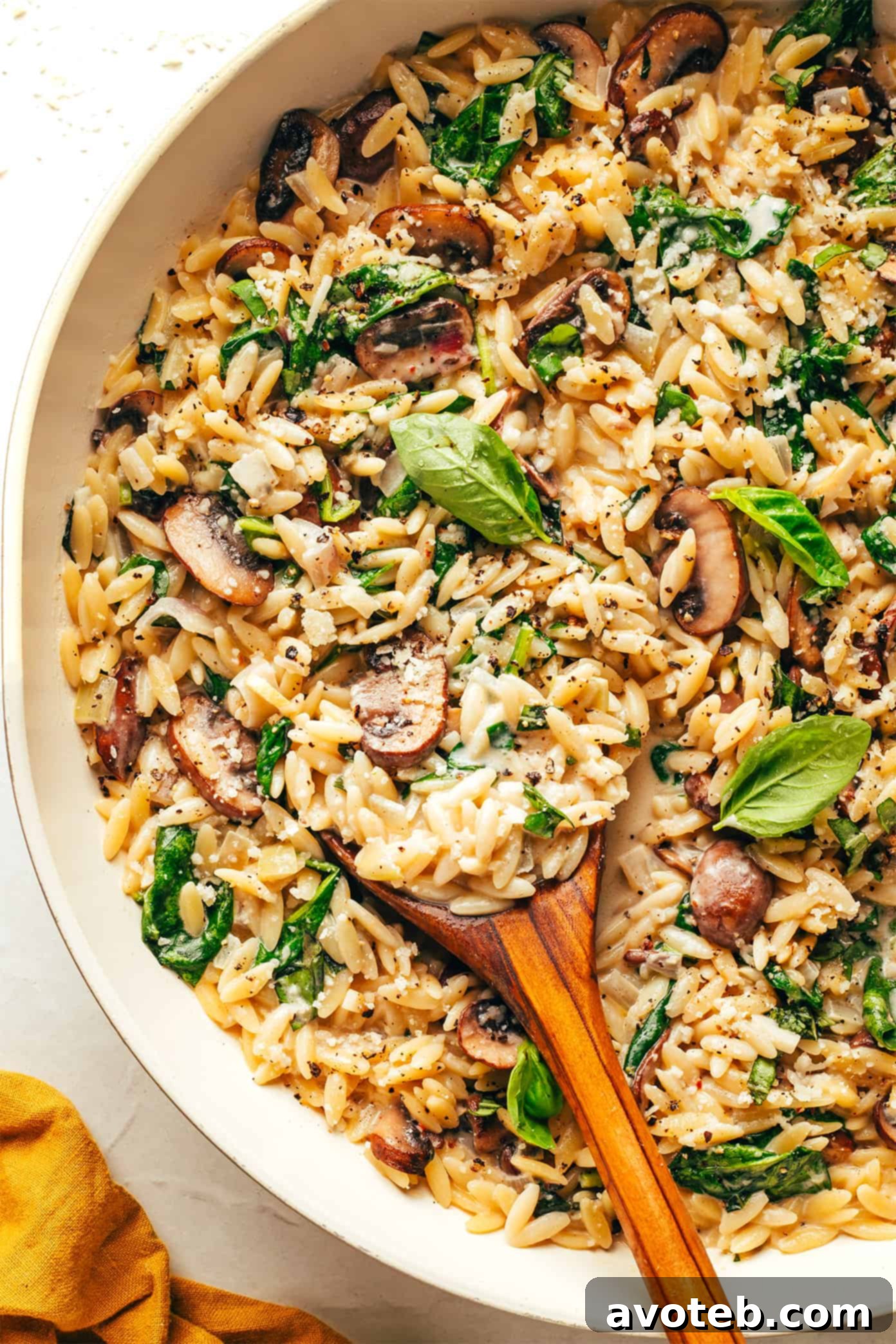 A serving of creamy garlic mushroom orzo pasta, with a fork digging in, showing the rich, creamy sauce.