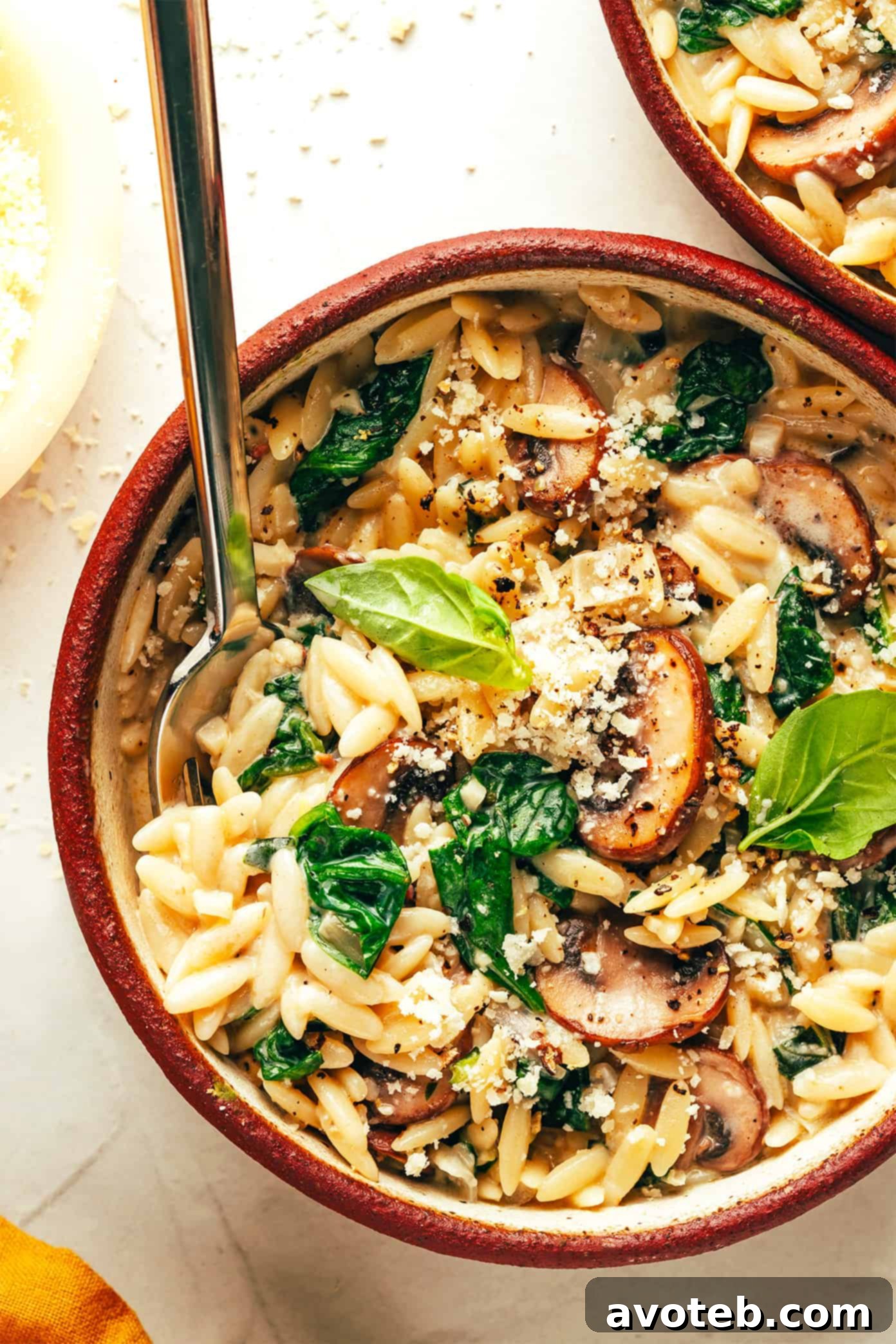 A wider shot of the creamy garlic mushroom orzo pasta in a bowl on a rustic wooden surface, with a spoon.