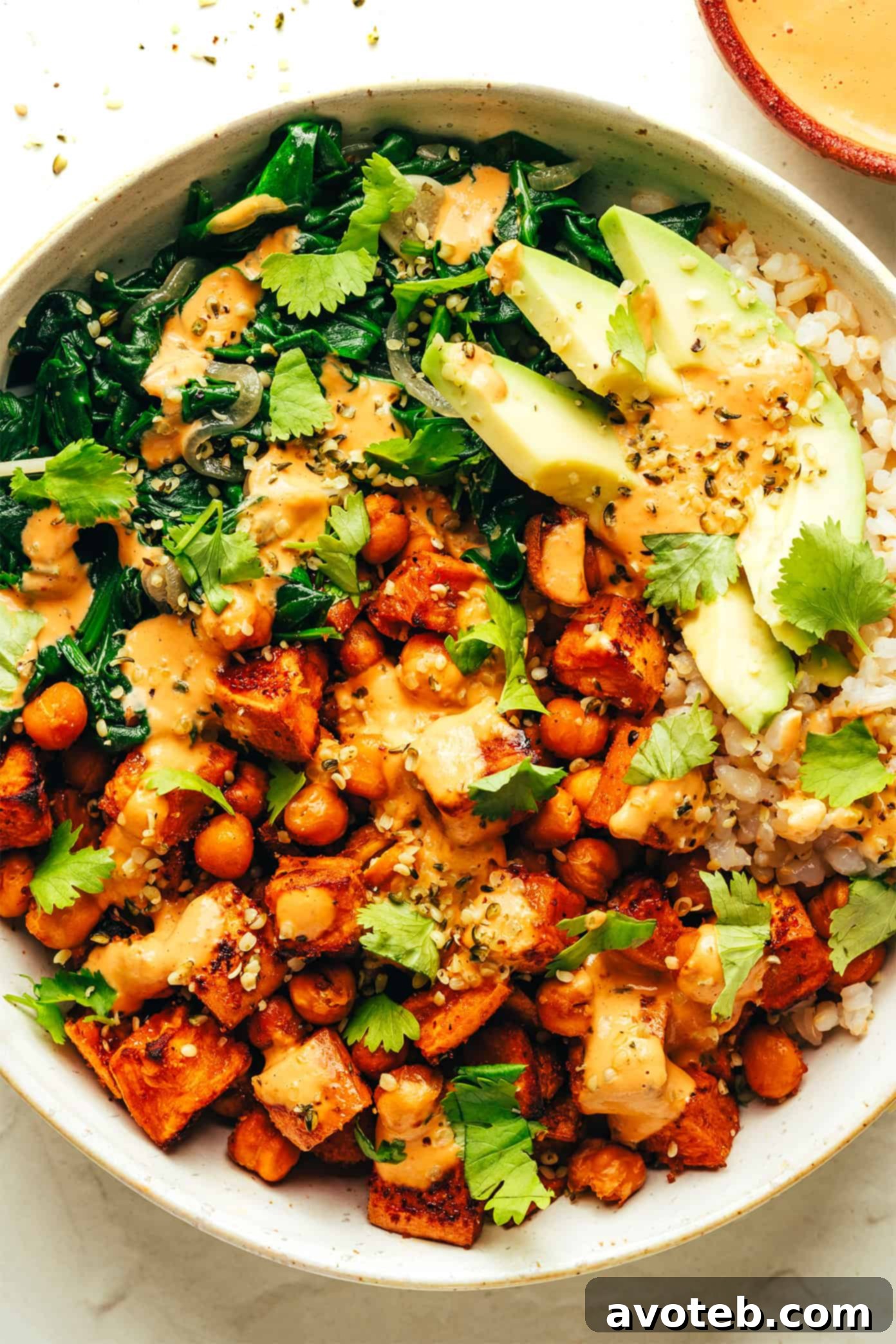 A beautifully plated roasted sweet potato and chickpea bowl with creamy avocado and fresh cilantro.