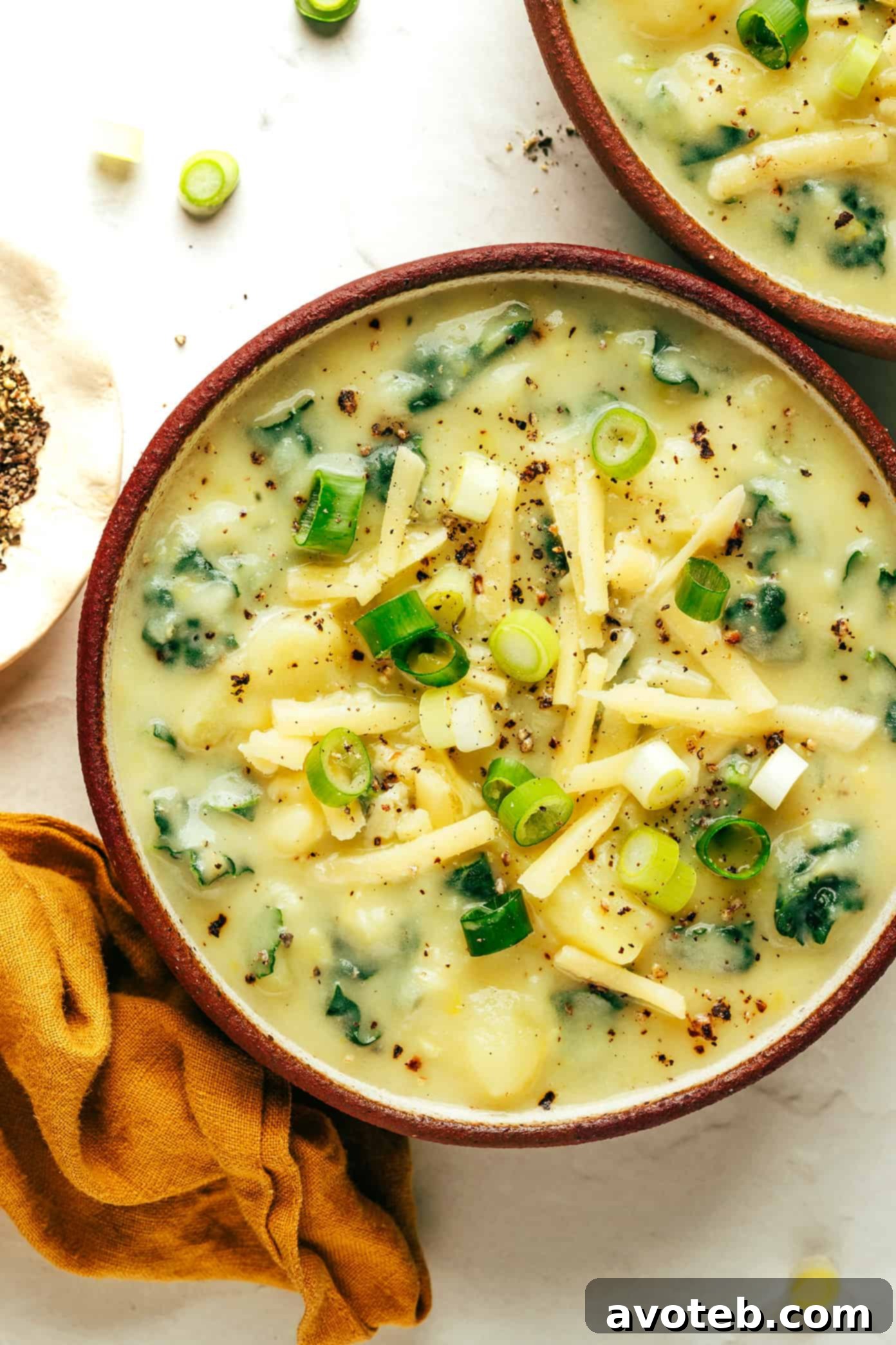 A bowl of creamy Colcannon Soup, topped with fresh scallions and a generous amount of shredded cheddar cheese.