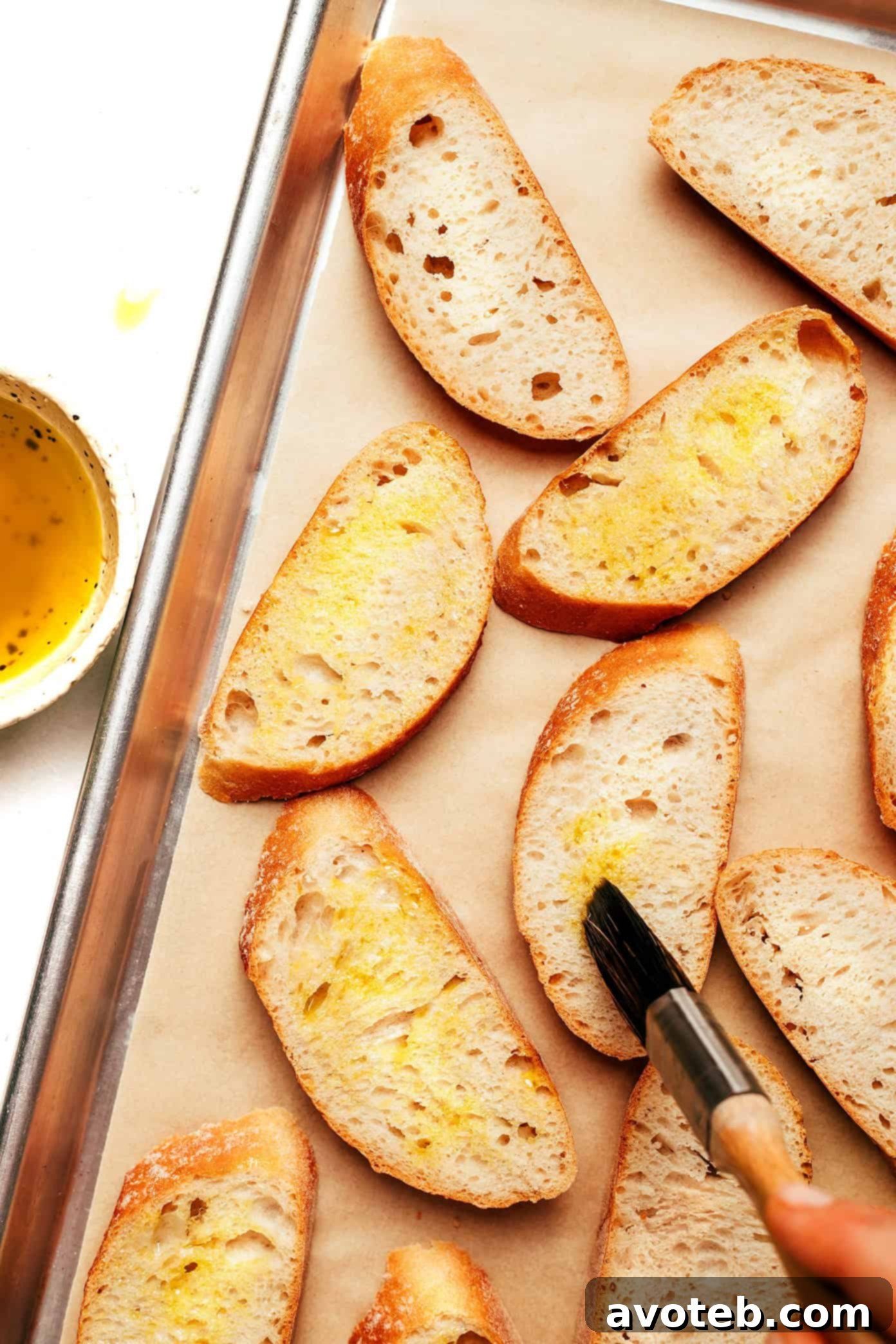 Close-up of three crostini slices, drizzled with olive oil and sprinkled with flaky sea salt, on a baking sheet before going into the oven.
