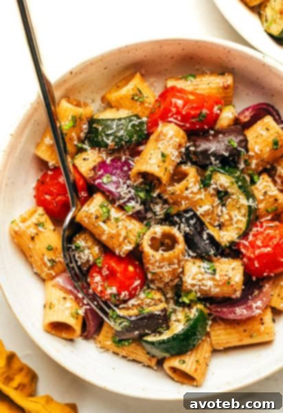 A bowl of roasted vegetable pasta with fresh basil and cheese.