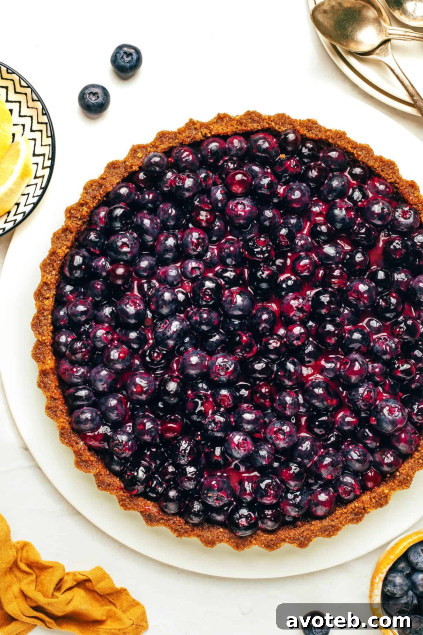 A beautifully sliced piece of no-bake blueberry tart on a white plate, revealing the layers of crust and filling, garnished with a fresh sprig of mint.