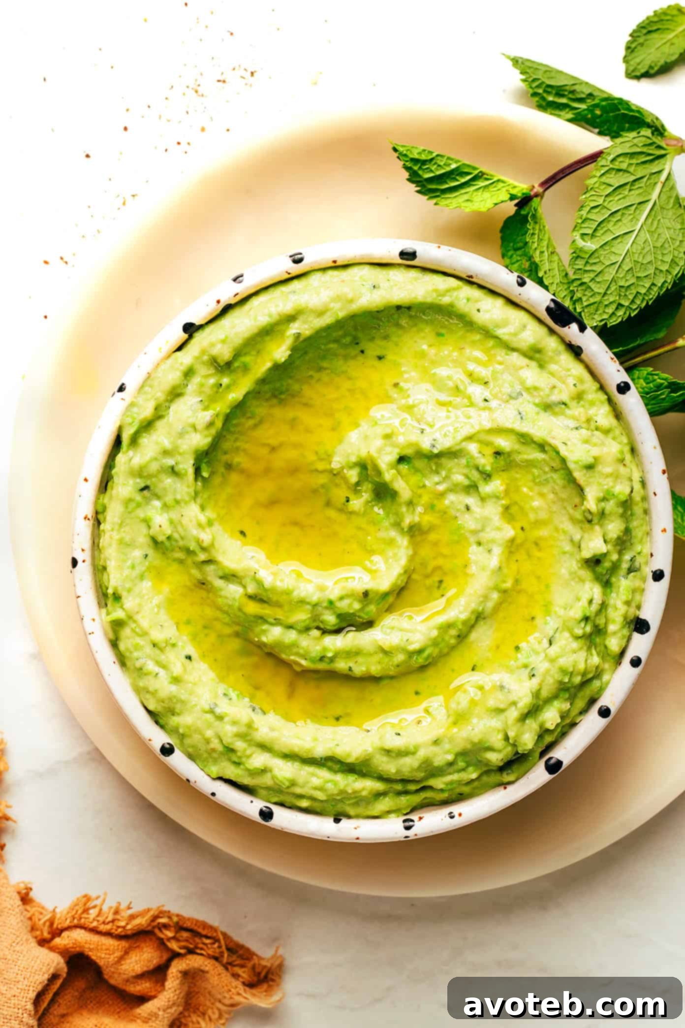 Vibrant Mint Pea Hummus 5 A beautifully composed shot of mint pea hummus, showing its creamy texture, with fresh mint and olive oil garnish. There are also crackers and raw vegetables like carrots and cucumbers for dipping.