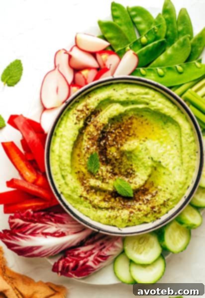 A vibrant bowl of homemade Mint Pea Hummus, garnished with fresh mint leaves and a swirl of olive oil, ready to be served.
