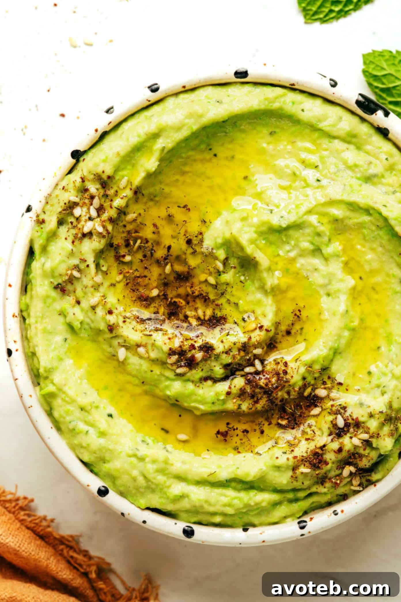 Vibrant Mint Pea Hummus 7 A final photo of the mint pea hummus in a serving bowl, perfectly smooth and garnished, surrounded by fresh ingredients like mint sprigs, lemons, and whole chickpeas.