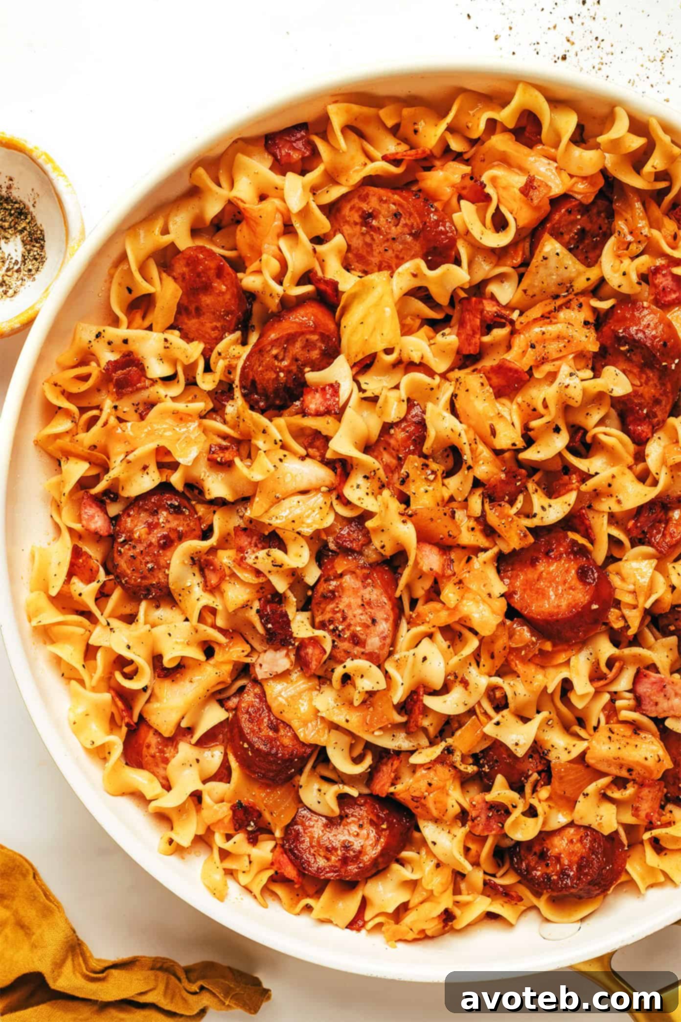 A close-up of a serving of kielbasa and cabbage noodles in a white bowl, garnished with fresh herbs, ready to be eaten.