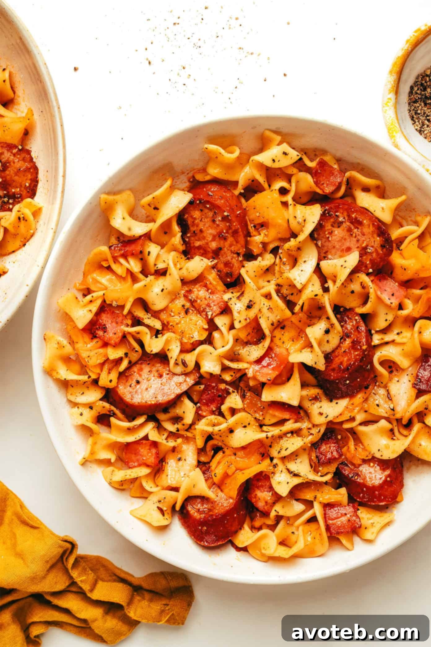 A rustic wooden table setting with a large serving bowl of kielbasa and cabbage noodles, alongside some fresh bread, creating a cozy meal scene.