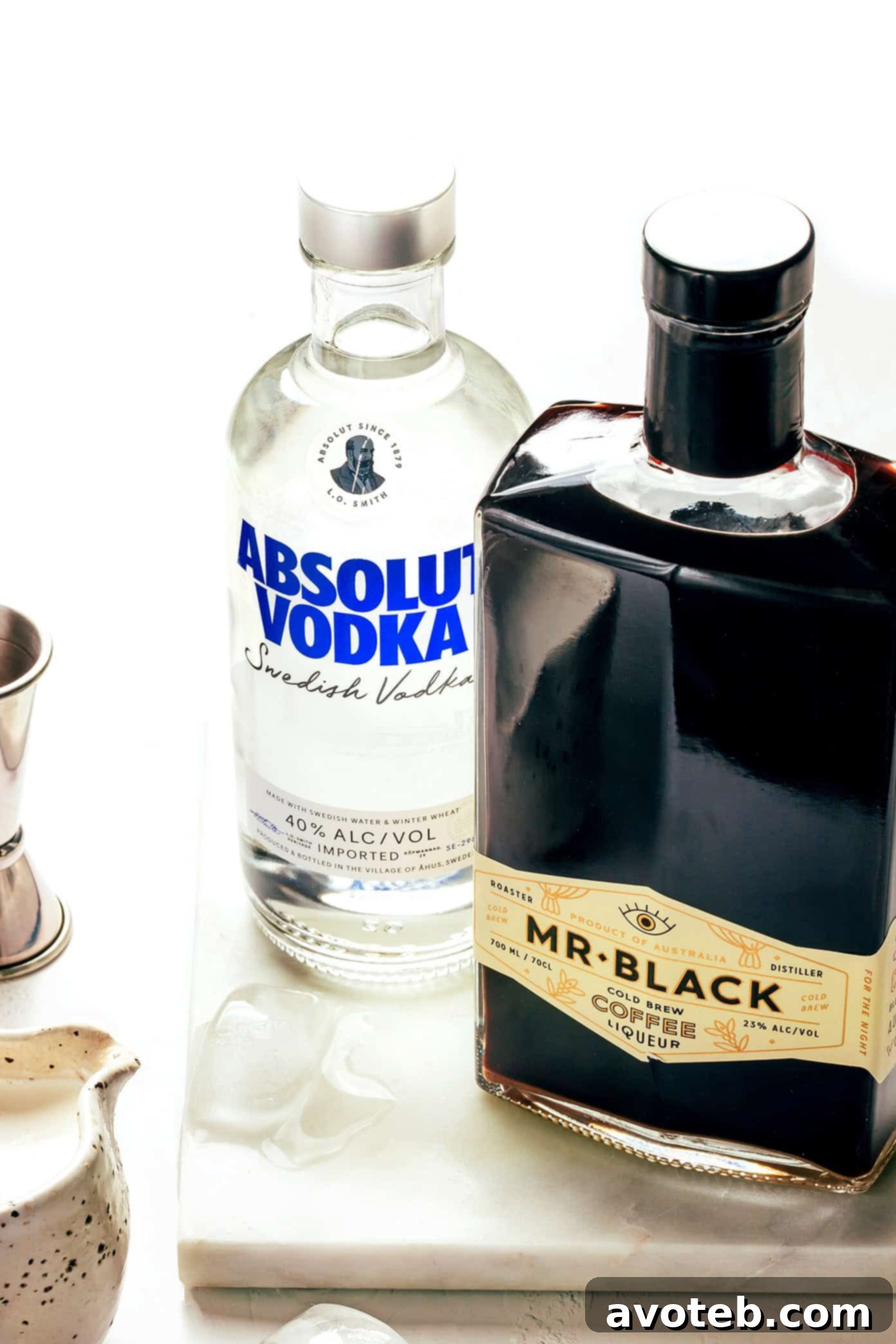 Two glasses of White Russian cocktails being prepared with bottles of vodka and Kahlúa