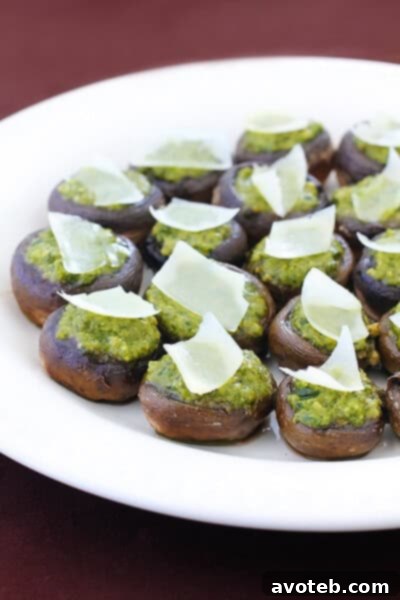 Two hands holding a platter of freshly baked pesto stuffed mushrooms with garnishes.