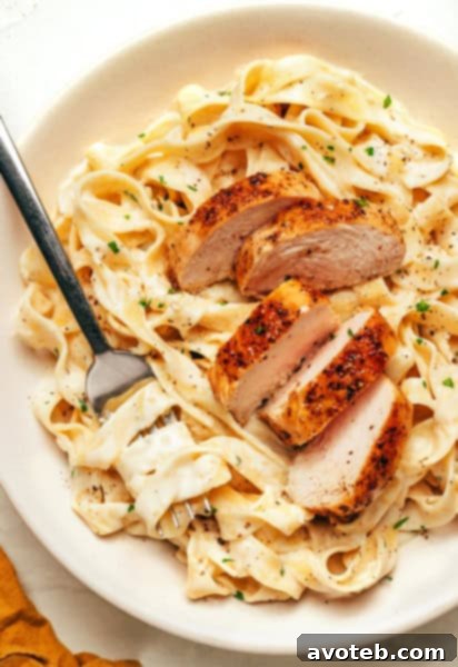 Chicken Fettuccine Alfredo in a white bowl with a fork, ready to be enjoyed.