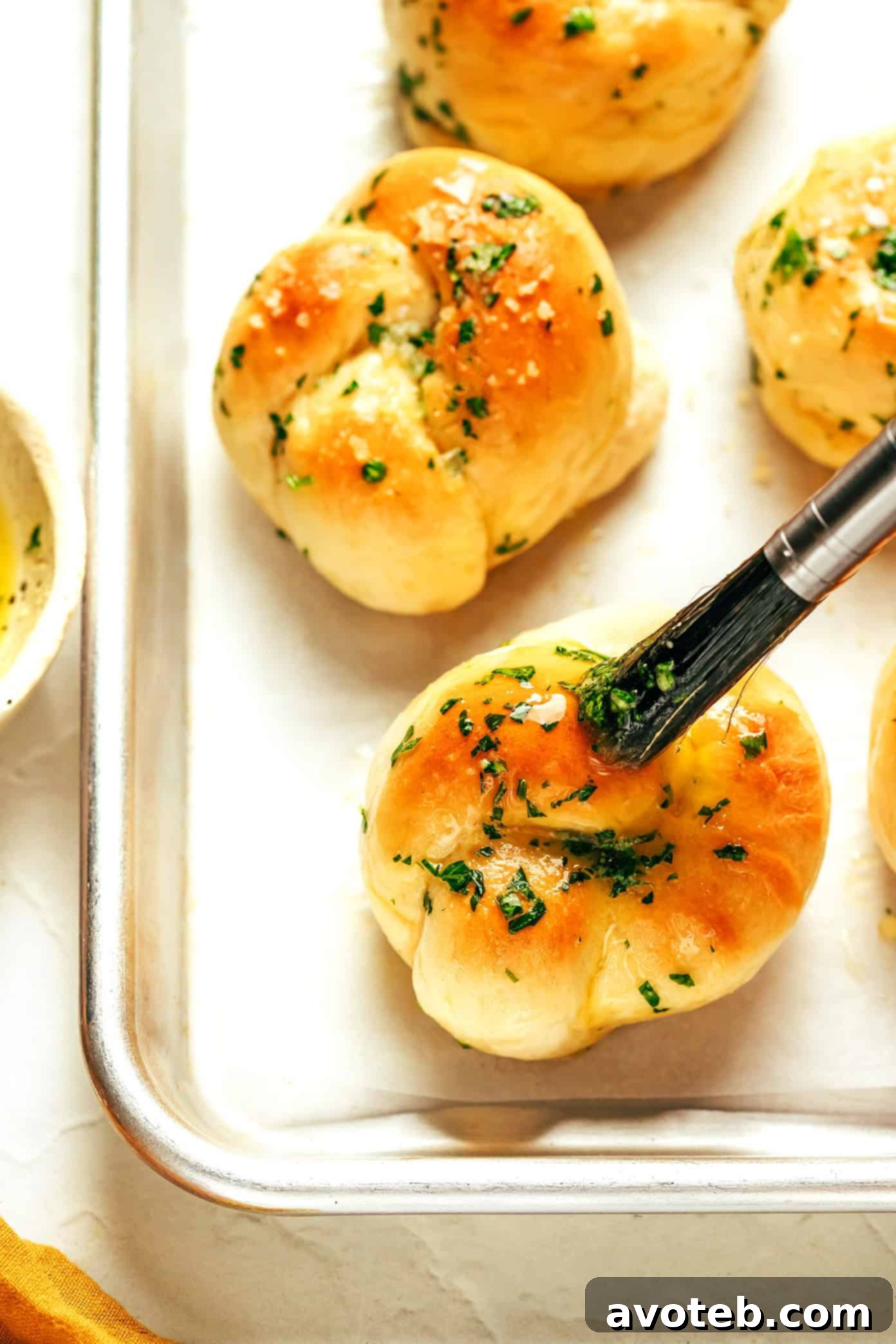 A close-up shot of garlic knots being brushed with melted garlic butter and sprinkled with Parmesan cheese.