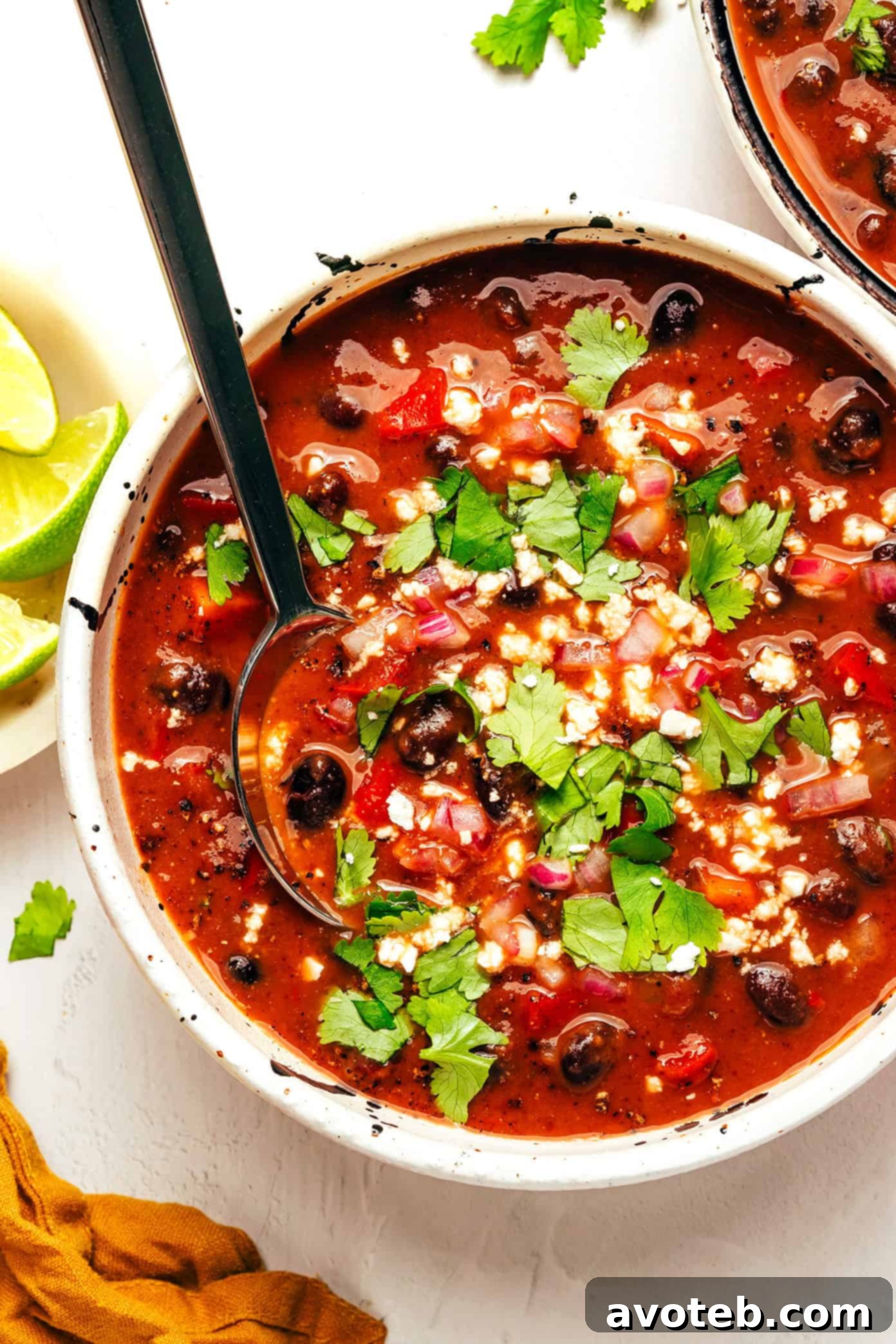A bowl of vegetarian black bean soup garnished with fresh cilantro, avocado, and red onion