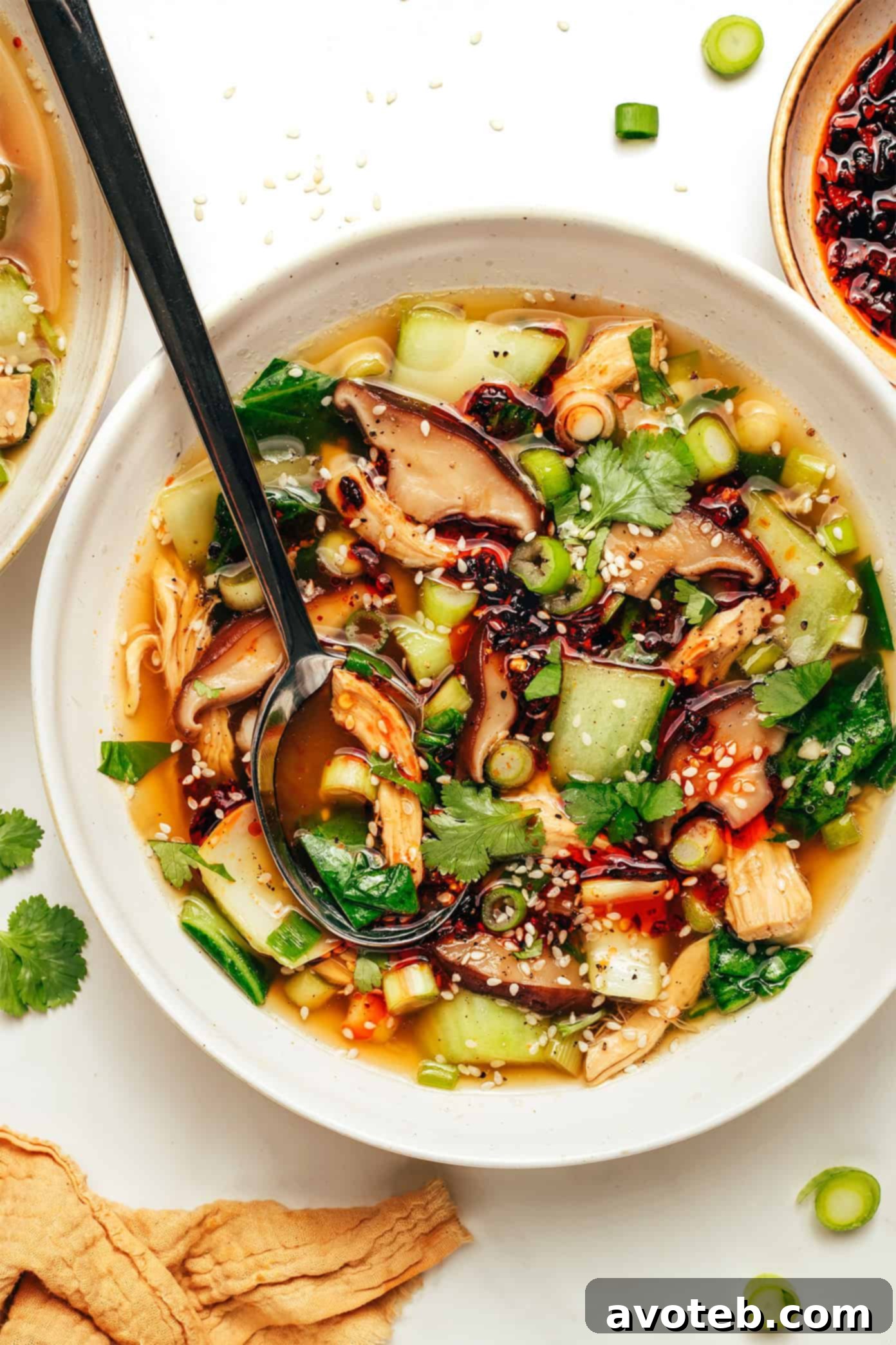 A steaming bowl of ginger scallion chicken soup, garnished with fresh cilantro and chili crisp, set against a rustic background.