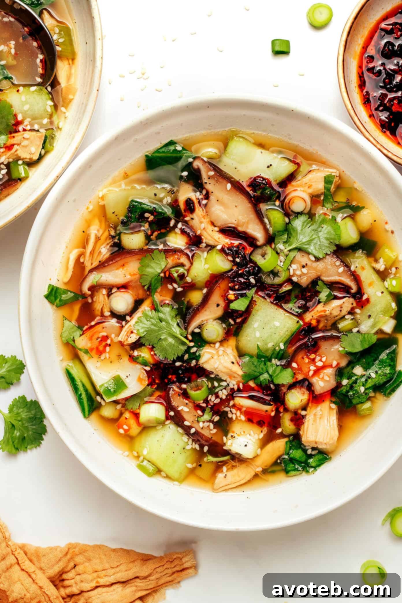 An overhead shot of ginger scallion chicken soup garnished with fresh herbs and a drizzle of chili crisp, ready to eat.