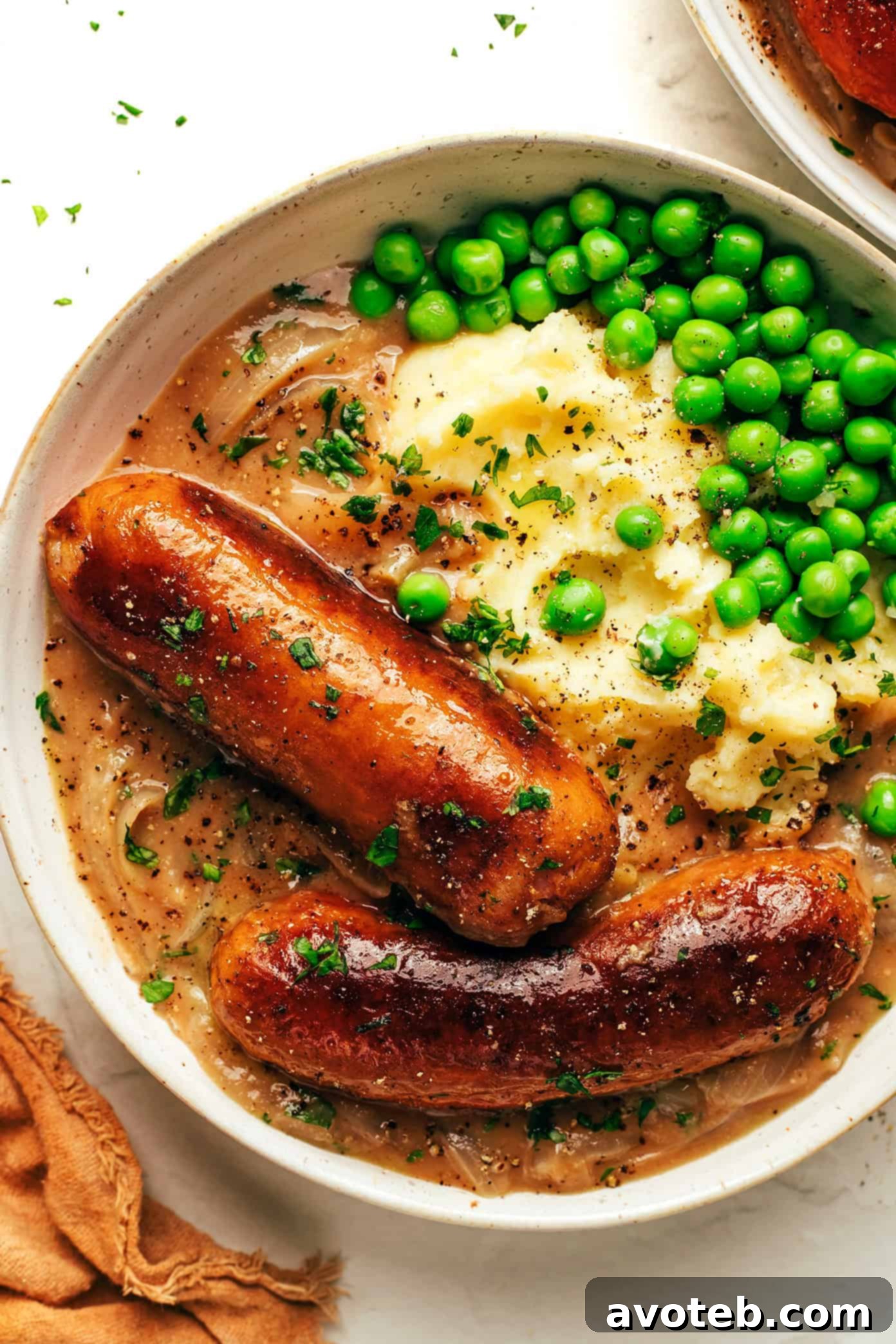 Bangers and Mash - A plate of golden-brown sausages served atop a bed of creamy mashed potatoes, generously covered with a rich, dark onion gravy, and garnished with fresh parsley.