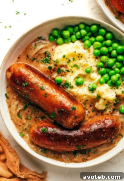 Bangers and Mash - A plate of golden-brown sausages served atop a bed of creamy mashed potatoes, generously covered with a rich, dark onion gravy, and garnished with fresh parsley.