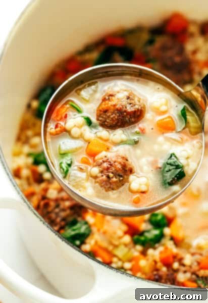 A steaming bowl of homemade Italian Wedding Soup with small meatballs, pasta, and spinach, garnished with fresh Parmesan cheese.