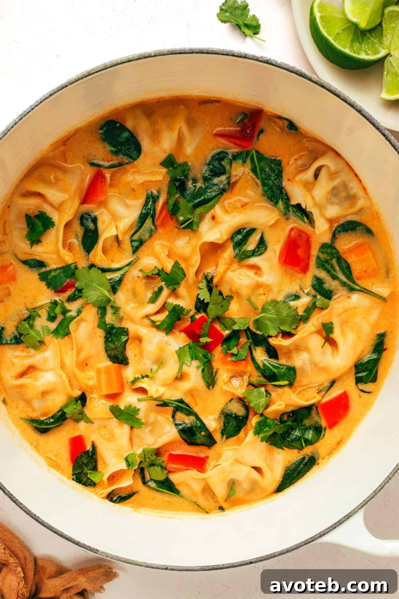 A bowl of Thai Red Curry Potsticker Soup ready to be served, with a spoon revealing a dumpling and vegetables.