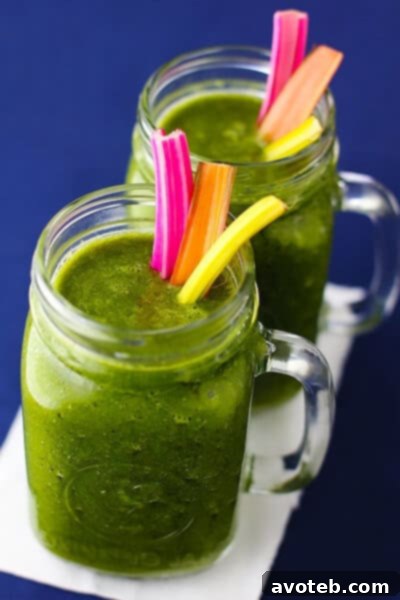 Two glasses of Rainbow Chard Banana Smoothie, beautifully presented with fresh chard leaves as garnish, on a rustic wooden table.