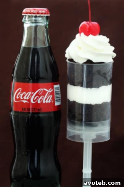 Coke Float Push-Up Pops | gimmesomeoven.com A close-up view of an assembled Coke Float Push-Up Pop, showcasing the alternating layers of moist Coca-Cola chocolate cake and creamy whipped topping, crowned with a vibrant stemmed maraschino cherry.