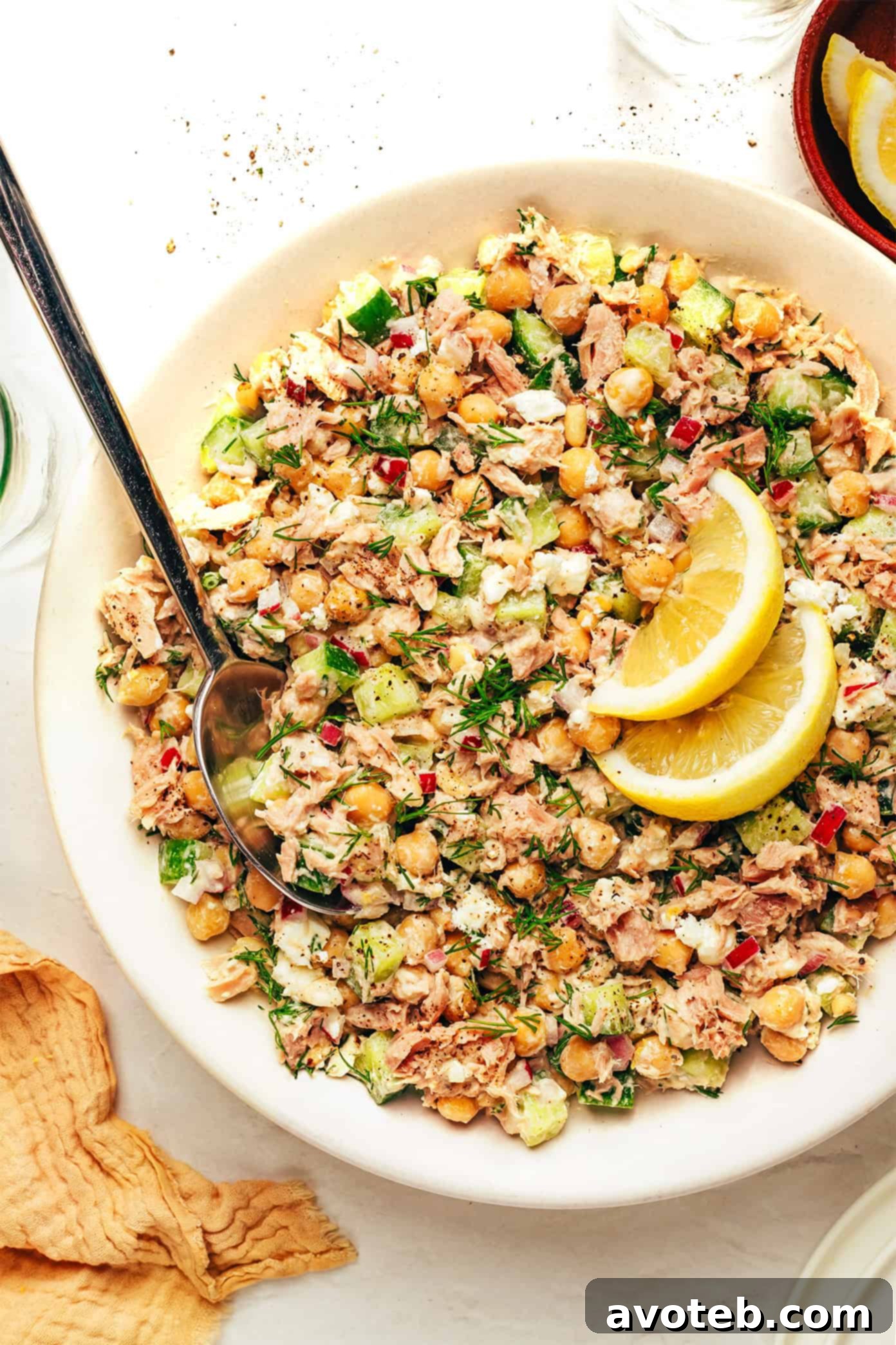 A beautifully presented bowl of Lemon Tahini Chickpea Tuna Salad, featuring a medley of chickpeas, flaked tuna, crisp cucumber, red onion, fresh dill, and crumbled feta, all glistening with a creamy tahini dressing.