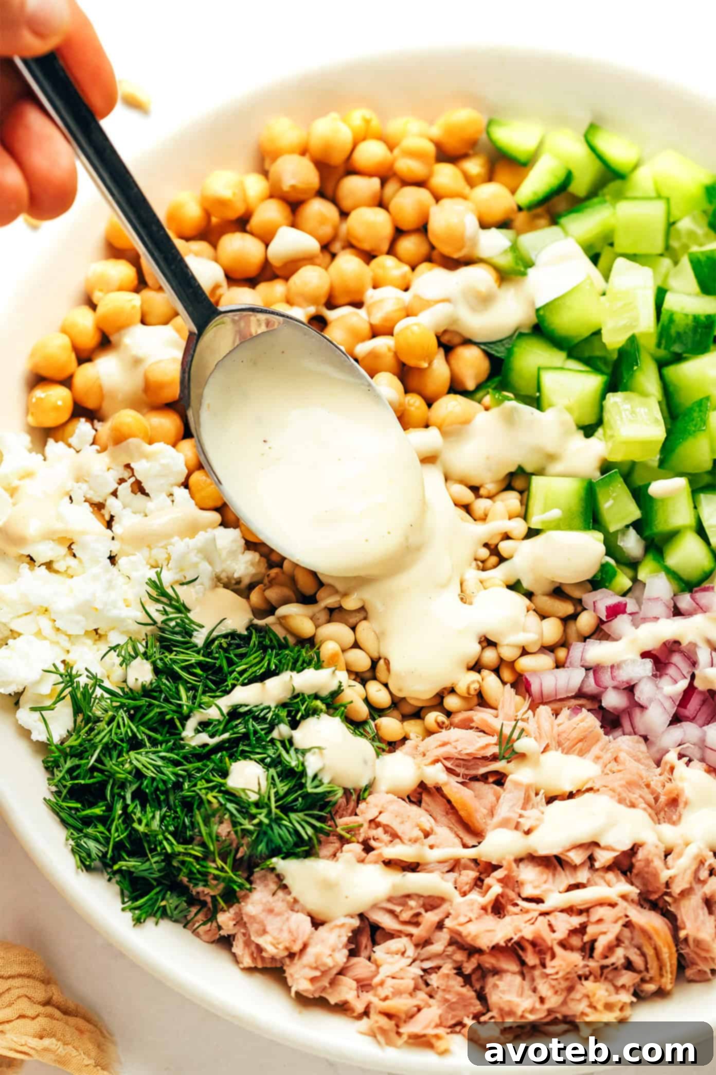 A bowl of fresh chickpeas, a can of olive oil-packed tuna, diced cucumbers, red onions, fresh dill, and crumbled feta, ready to be combined for the salad.