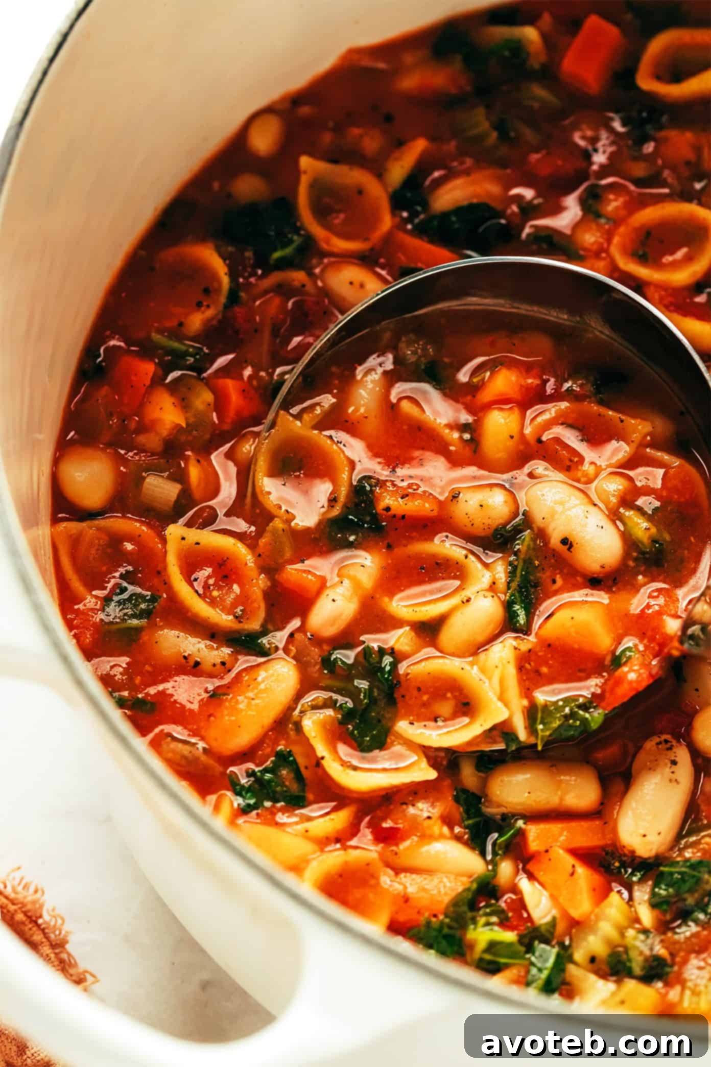 A large, steaming pot of Pasta e Fagioli soup, beautifully garnished with fresh basil leaves, ready to be served.