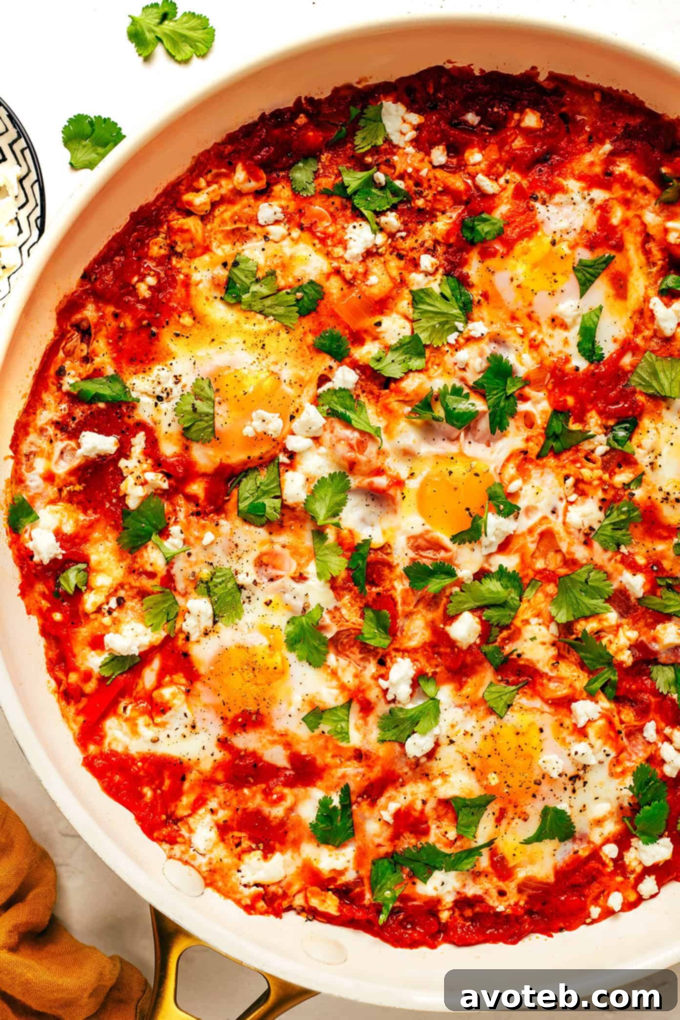 A vibrant pan of shakshuka, freshly garnished with feta cheese and chopped cilantro, ready to be enjoyed.