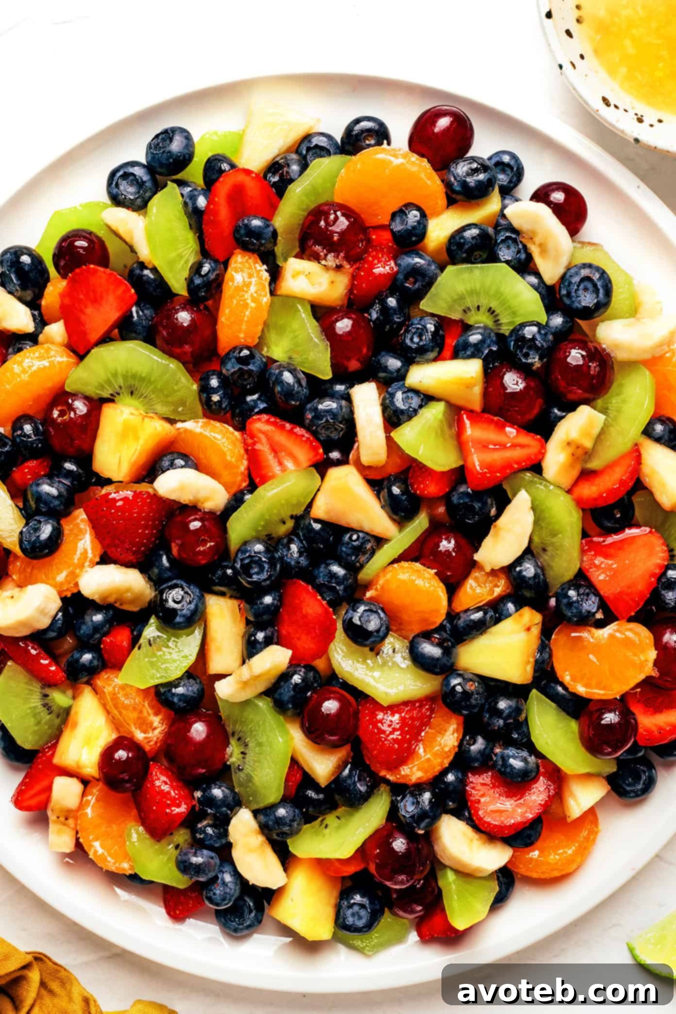 A vibrant, colorful fruit salad in a white bowl, showcasing a mix of berries, pineapple, grapes, and kiwi, garnished with a lime slice. It's the perfect colorful side dish for picnics, grill nights or summer dinners!