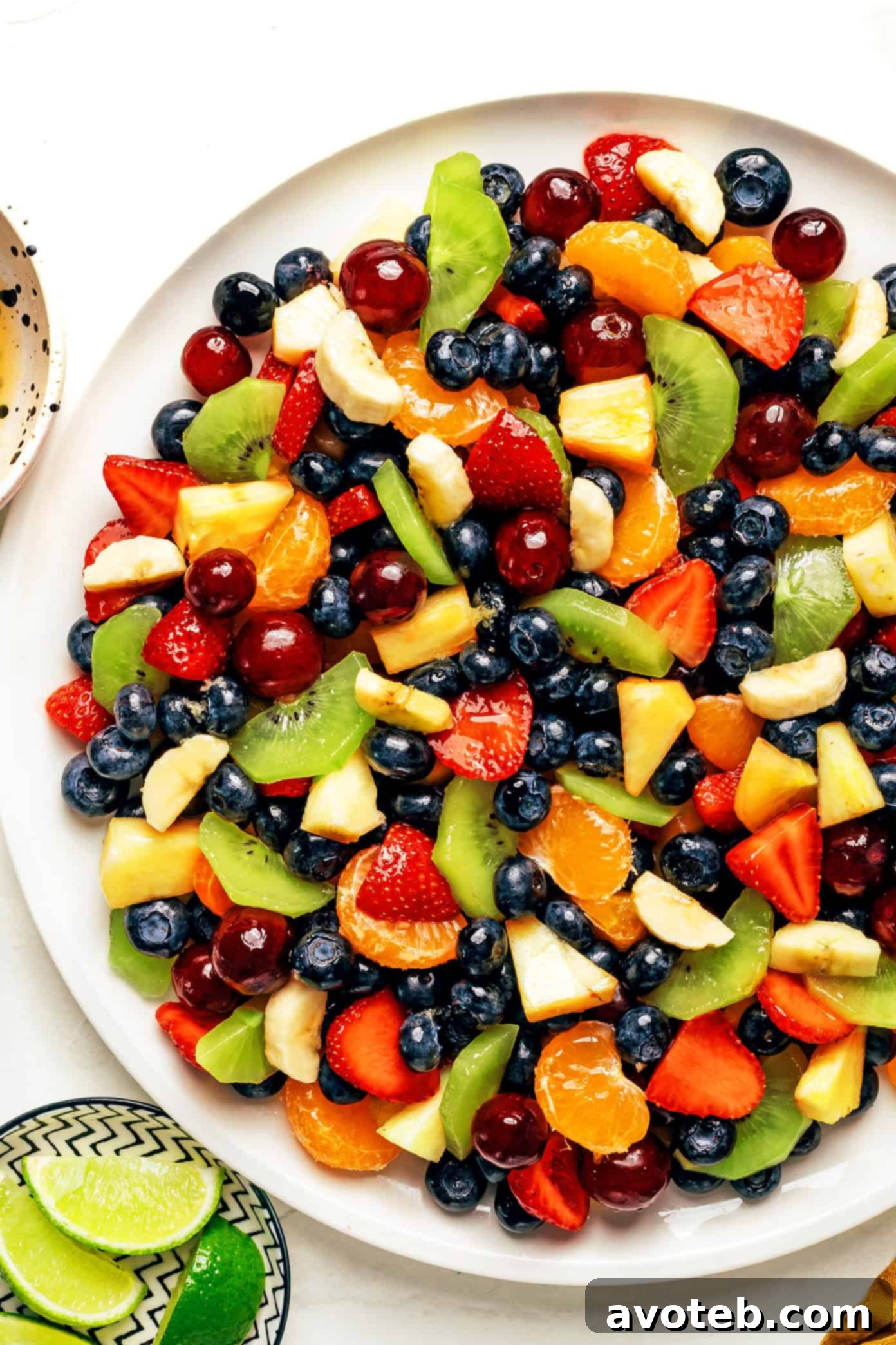 A large bowl of fruit salad with ginger-lime dressing drizzled over it, ready to be tossed. The fruits are glistening from the dressing.